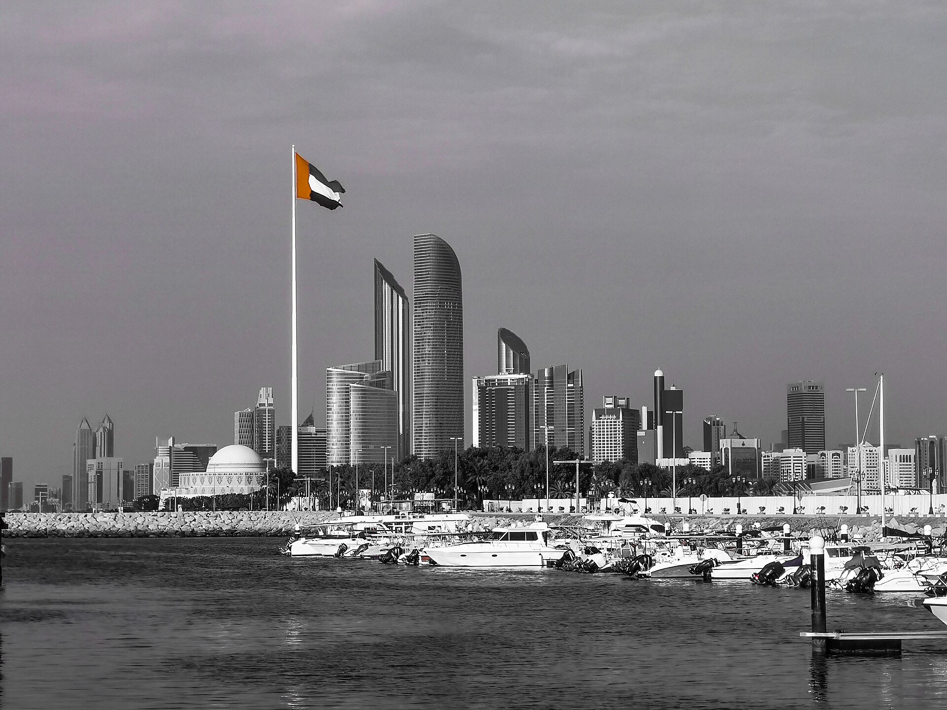 Abu Dhabi skyline with UAE national flag flying in the foreground, the Corniche waterfront and city towers behind, symbolising the UAE capital’s growing independence from Gulf institutional frameworks