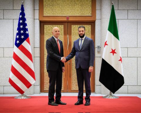US Special Envoy Tom Barrack shakes hands with Syrian President Ahmad al-Sharaa at the People's Palace in Damascus, May 2025, with US and Syrian flags in the background
