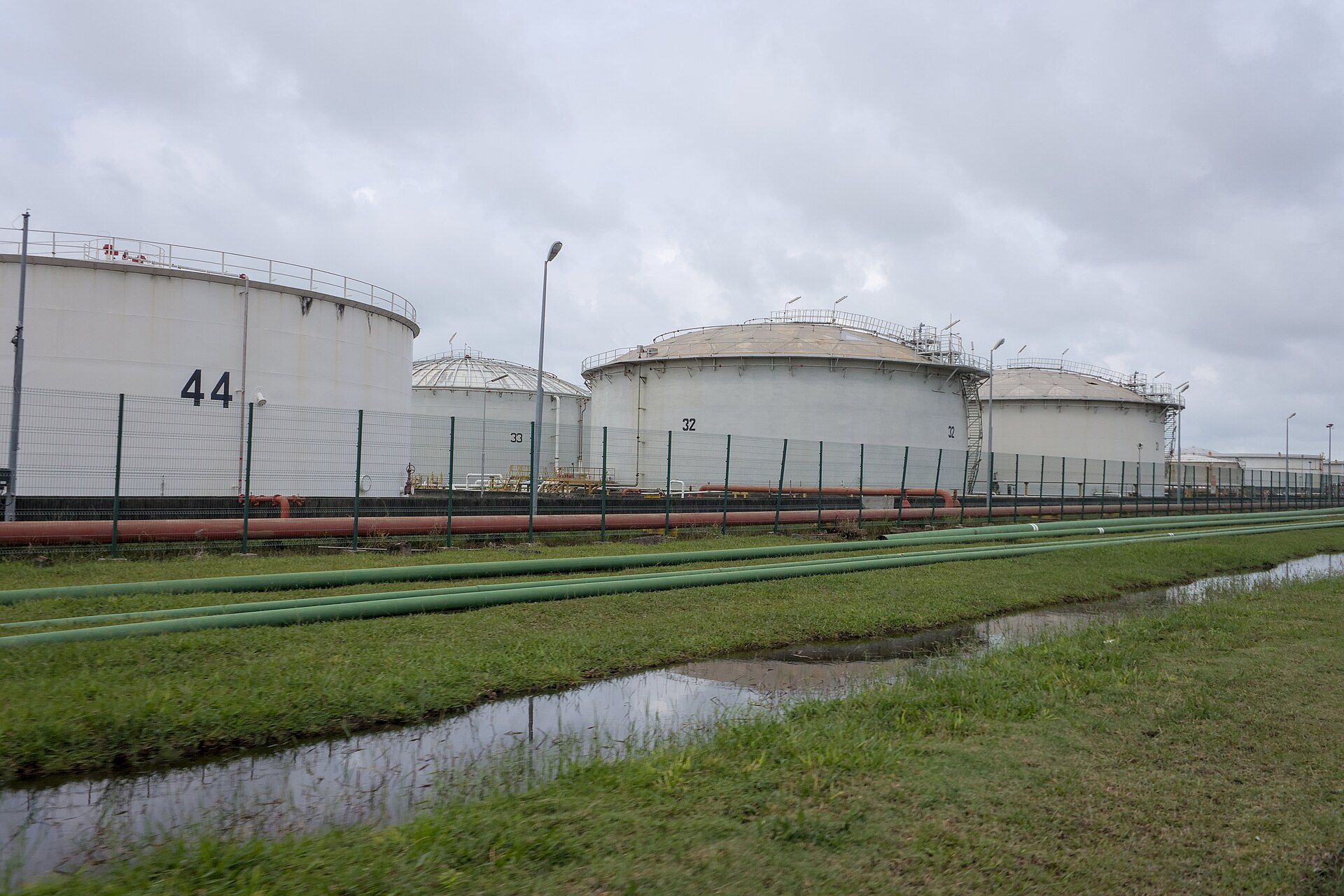 Large white petroleum storage tanks at a crude oil terminal, with pipeline manifolds visible at ground level — the type of fixed infrastructure that makes terminal facilities high-value targets in energy infrastructure strikes