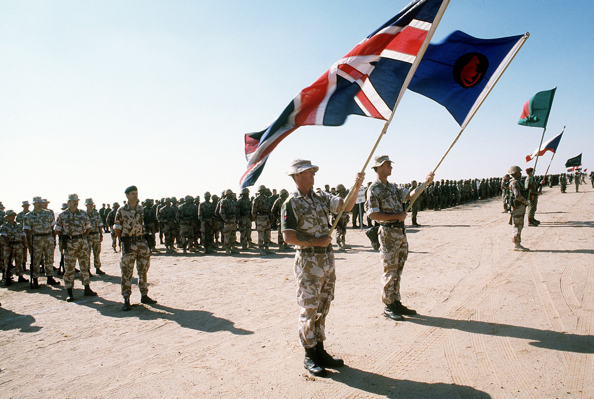 British troops and coalition forces gather for review by King Fahd of Saudi Arabia during Operation Desert Storm, 1991. The 1990 model — Kuwait request, Article 51 notification, UNSC Resolution 678 — set the legal template Saudi Arabia has not replicated since.