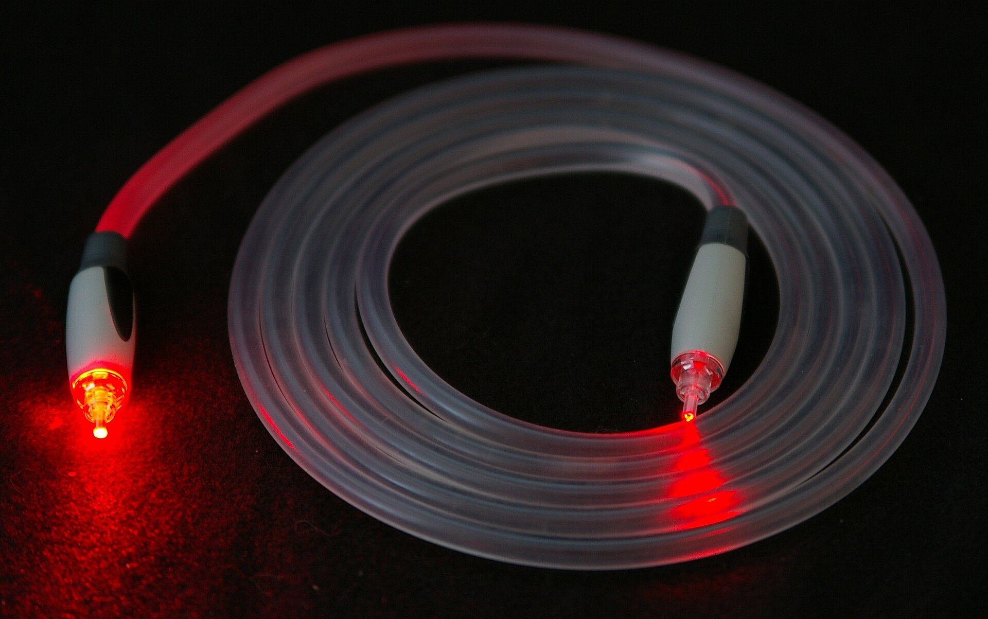 Illuminated optical fiber cable carrying red light signal, representing the STC Silk Link fiber-optic network being built across Syria