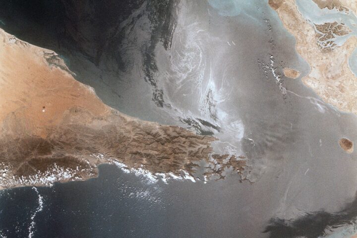 NASA Space Shuttle aerial view of the Strait of Hormuz showing ship wakes, Iran coastline, and the Musandam Peninsula narrows — the 21-nautical-mile passage at the center of Iran's sovereignty claim