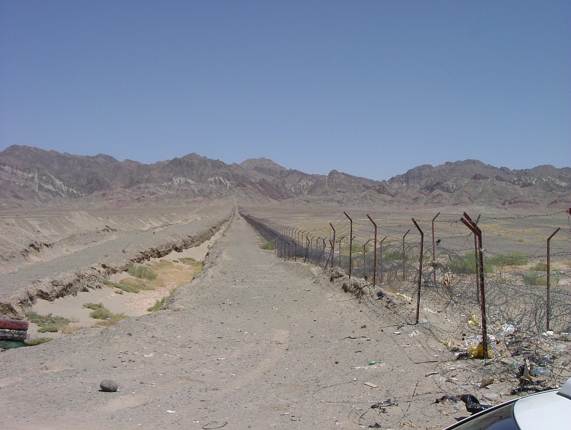 The Iran-Pakistan border fence stretching across the Balochistan desert toward mountain ranges, showing the ~900km frontier between the two countries