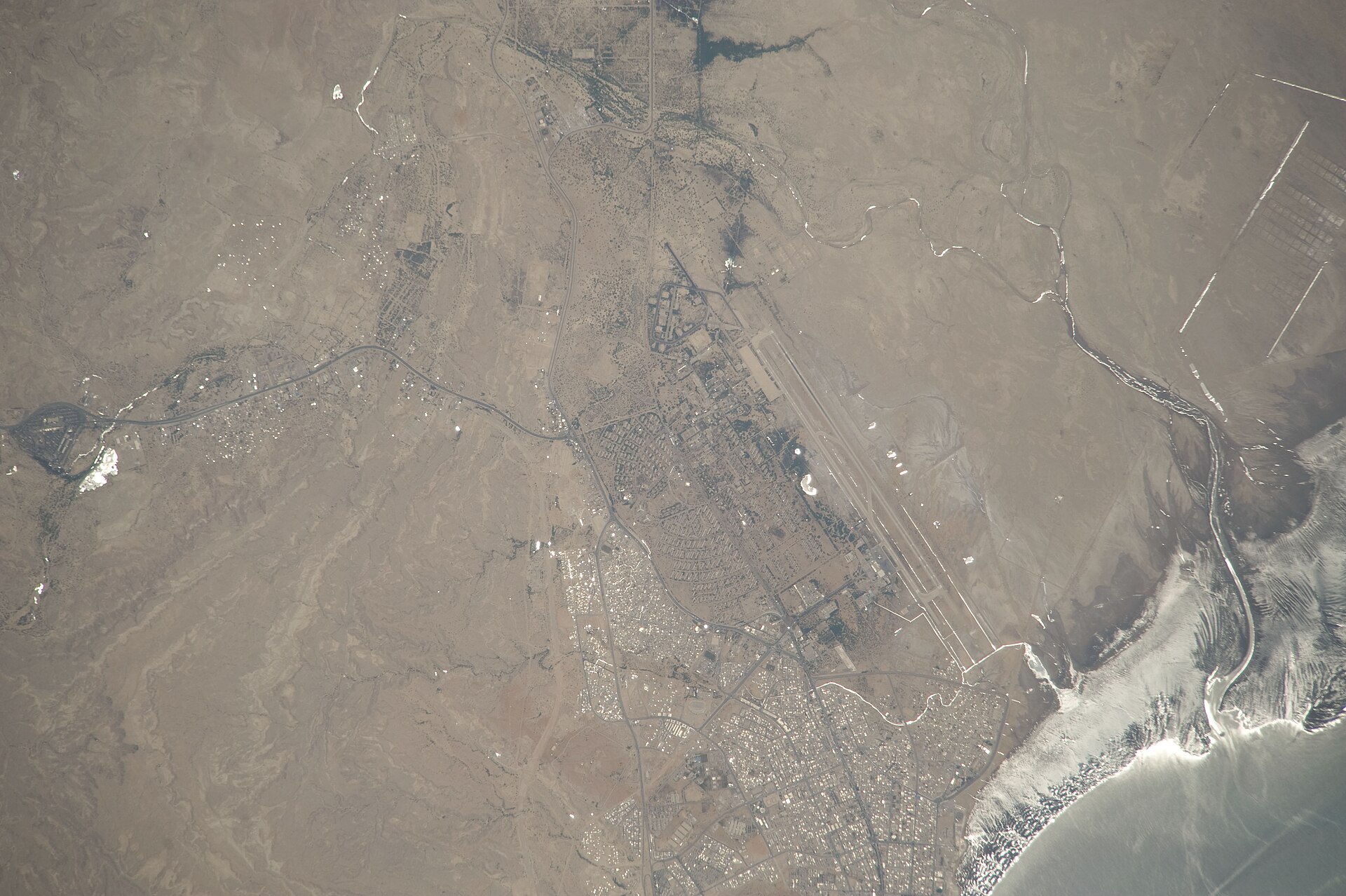 ISS astronaut photograph of Bandar Abbas, Iran, showing the city, its dual-use military-civil airbase, and the Persian Gulf coastline — the western anchor of the IRGC Aerospace Force Hormuz corridor missile network