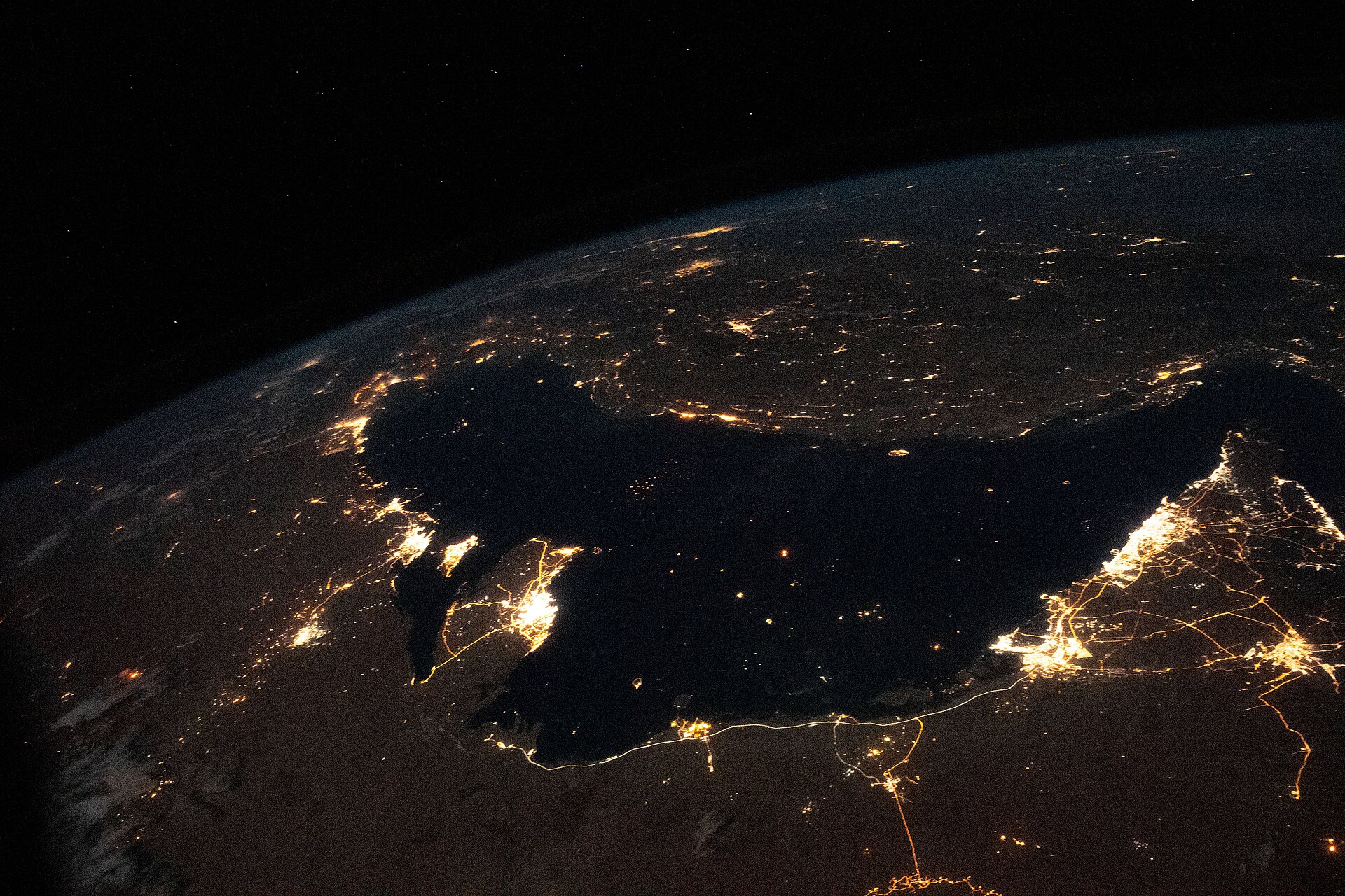 International Space Station photograph of the Persian Gulf at night — the bright industrial corridor along Saudi Arabia's Eastern Province shoreline marks the Dammam-Dhahran-Ras Tanura petroleum complex that SANG's Eastern Province command is tasked with protecting