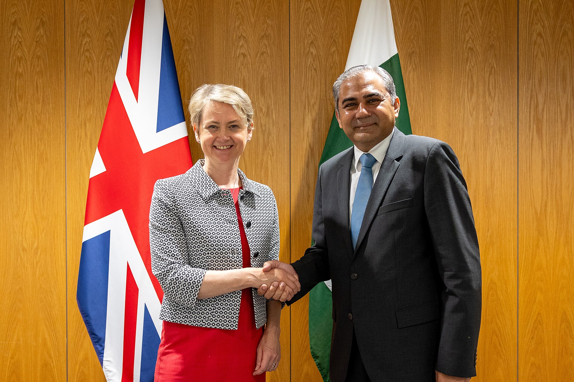 Pakistan Interior Minister Mohsin Naqvi shakes hands with UK Home Secretary Yvette Cooper in London, August 2024, in front of Pakistani and UK flags