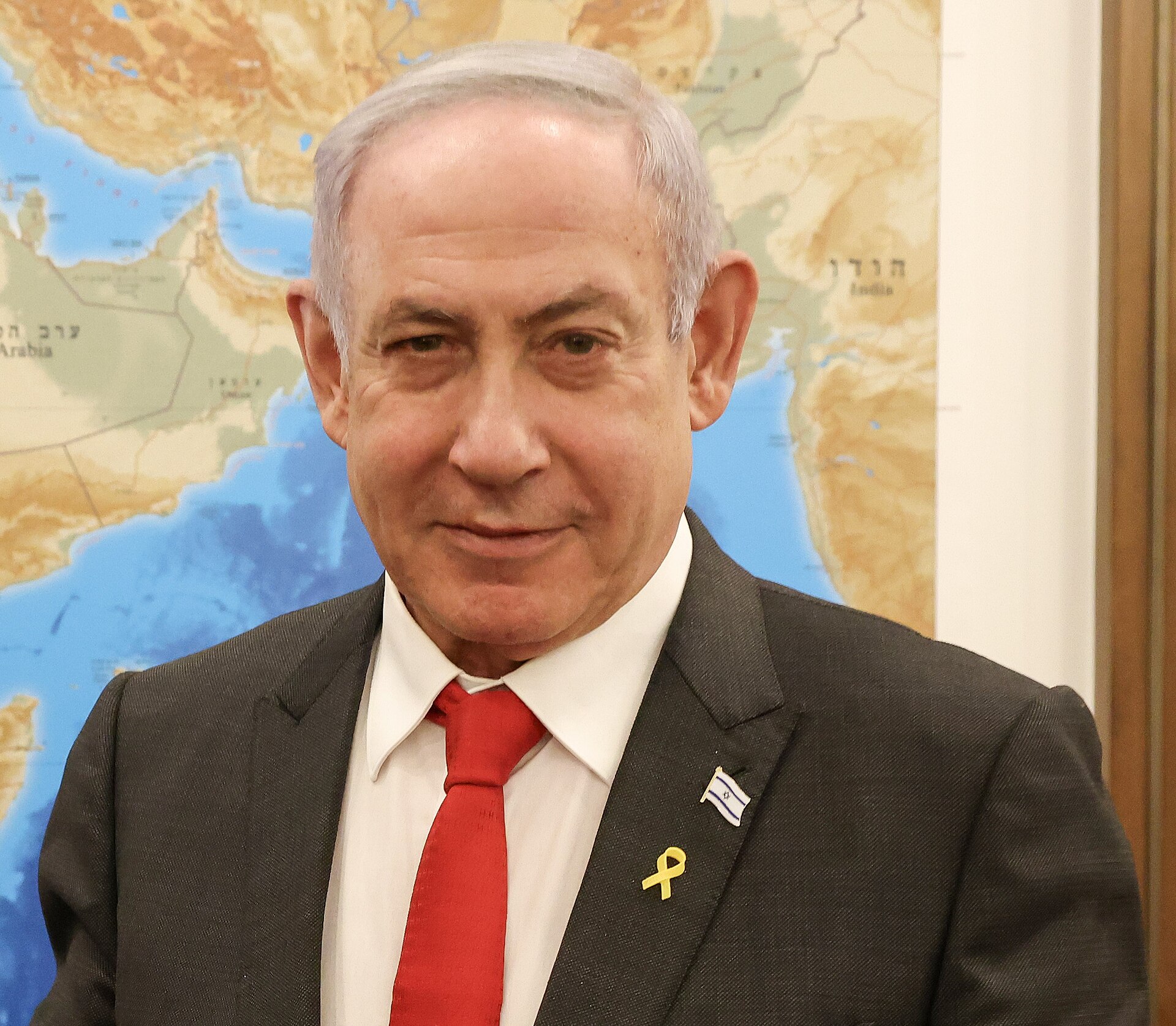 Israeli Prime Minister Benjamin Netanyahu stands before a Middle East map, January 2024, wearing an Israeli flag lapel pin and yellow hostage ribbon