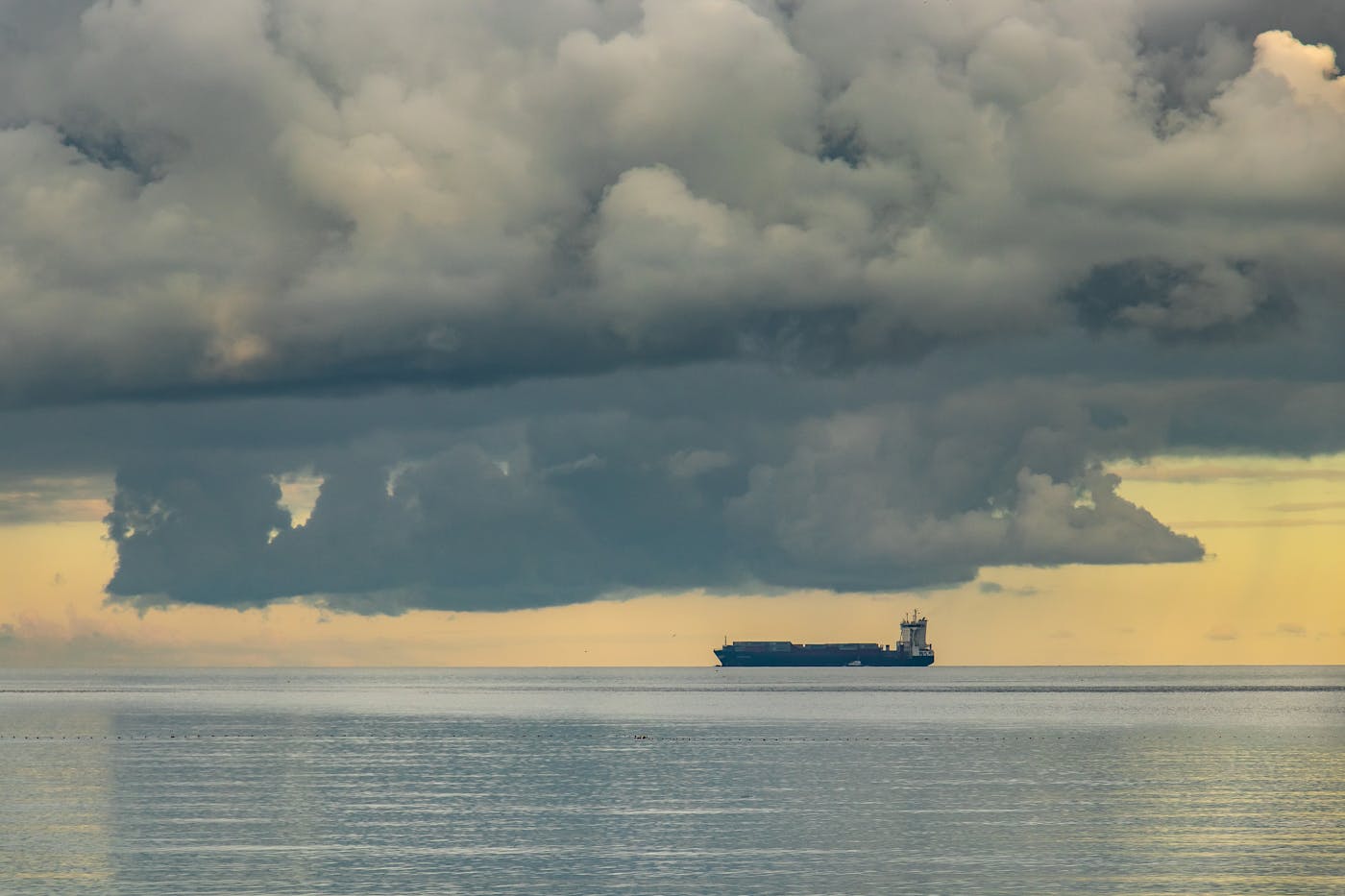 A cargo vessel on the sea horizon under approaching storm clouds. Saudi Arabia rerouted crude exports through Yanbu on the Red Sea after Hormuz closed, handling approximately 5 million barrels per day.