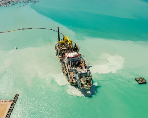 Dredging vessel working on port construction in turquoise waters, with breakwater quay visible — the type of marine construction that built Oxagon's 4.6 km quay wall