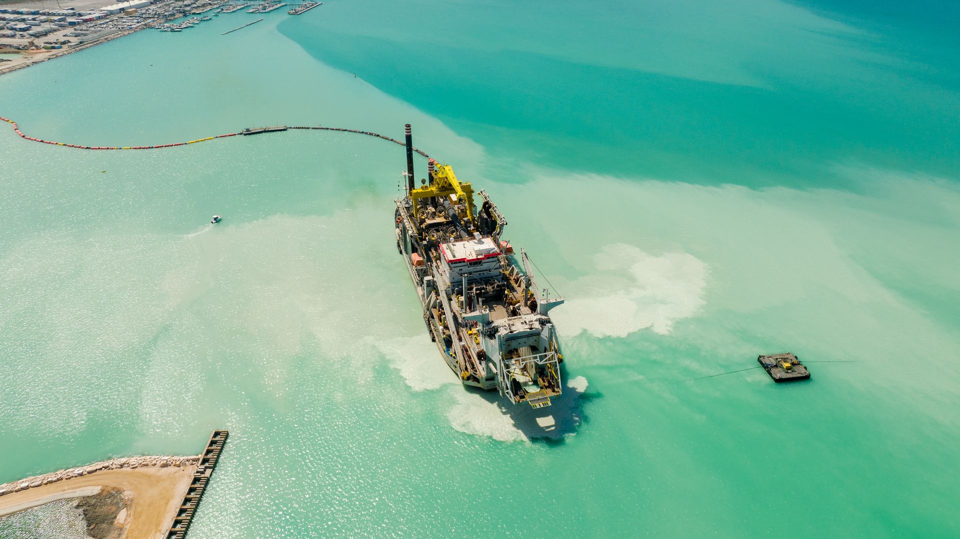 Dredging vessel working on port construction in turquoise waters, with breakwater quay visible — the type of marine construction that built Oxagon's 4.6 km quay wall