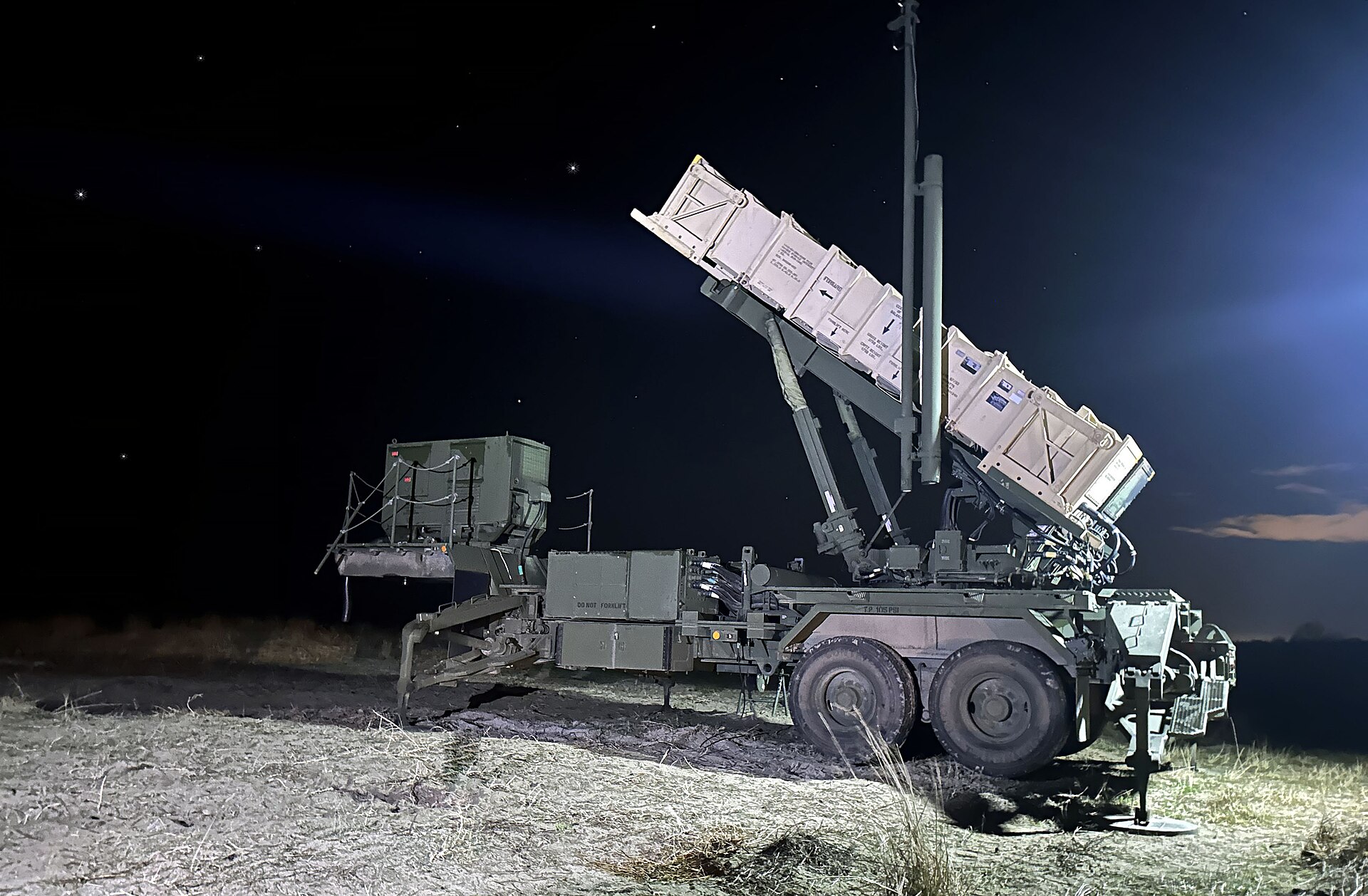 A Patriot missile launcher deployed at night during Romania live-fire exercise, launcher arm elevated and missile canisters loaded, stars visible behind