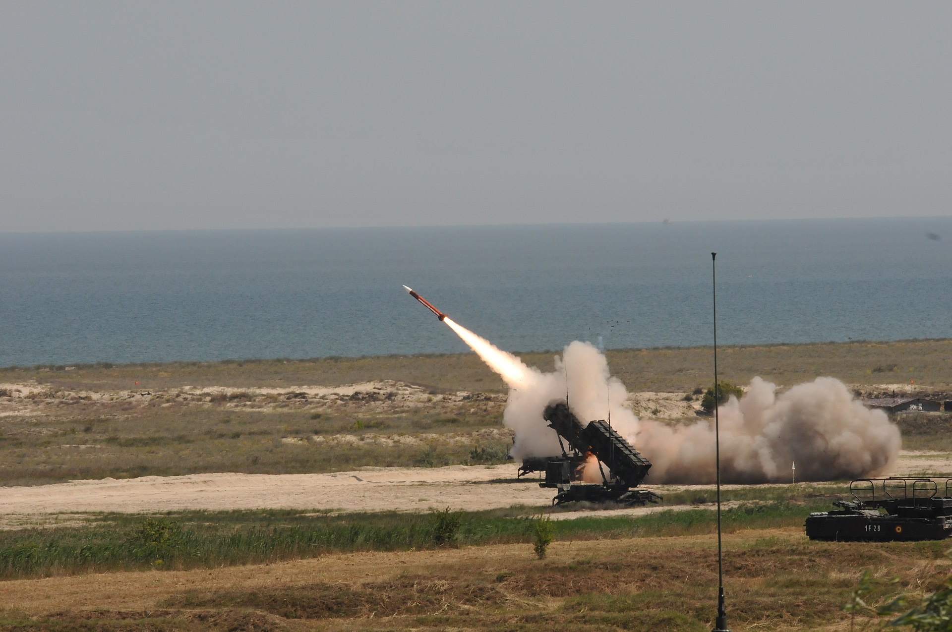 A PAC-3 Patriot missile system fires an interceptor at a live-fire range, with smoke billowing from the launcher. The UAE deploys Patriot PAC-3 batteries as part of its layered air defence against Iranian ballistic missiles and drones.
