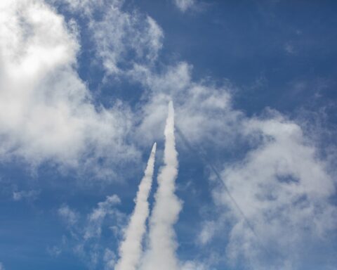 Two Patriot PAC-2 interceptor missiles climbing skyward during a live-fire exercise, leaving parallel white contrails against blue sky