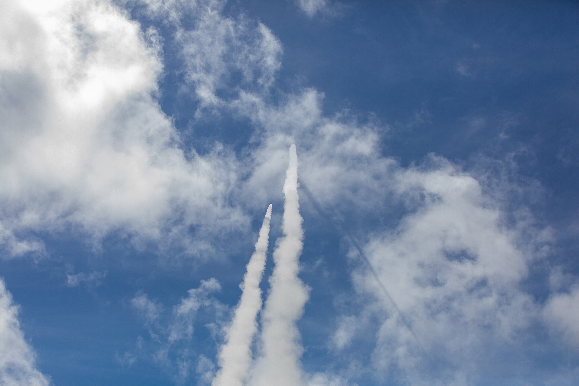 Two Patriot PAC-2 interceptor missiles climbing skyward during a live-fire exercise, leaving parallel white contrails against blue sky