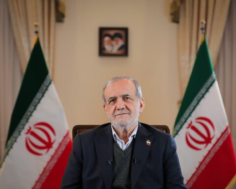 Iranian President Masoud Pezeshkian seated between two Iranian flags with Supreme Leader portraits on the wall, representing the institutional framework constraining civilian authority under Article 110