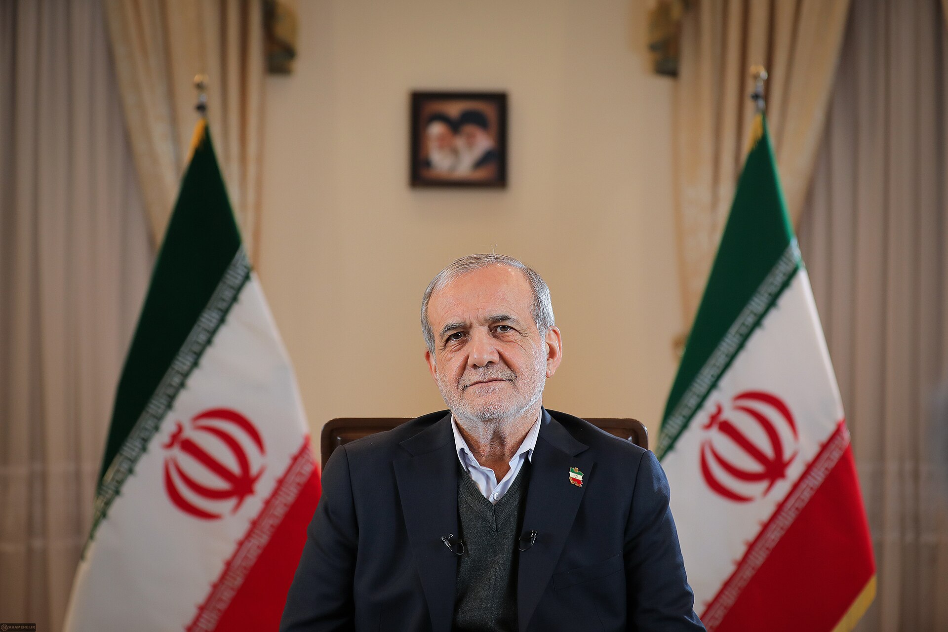 Iranian President Masoud Pezeshkian seated between two Iranian flags with Supreme Leader portraits on the wall, representing the institutional framework constraining civilian authority under Article 110