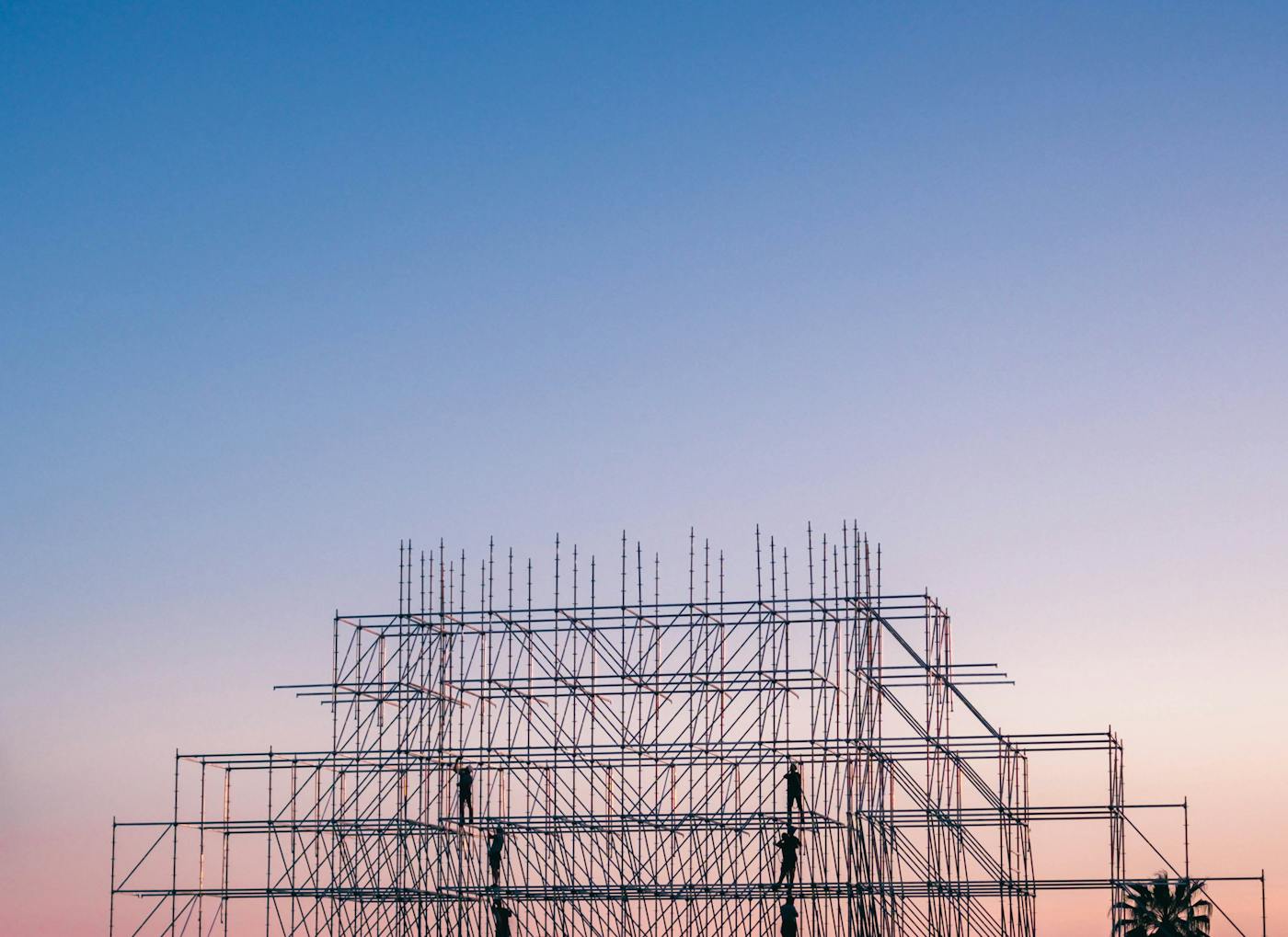 Construction workers on scaffolding at a large building site at dusk. PIF construction awards dropped from $71 billion to $30 billion before the war; the conflict provided a diplomatic cover story for a retreat that was already underway.