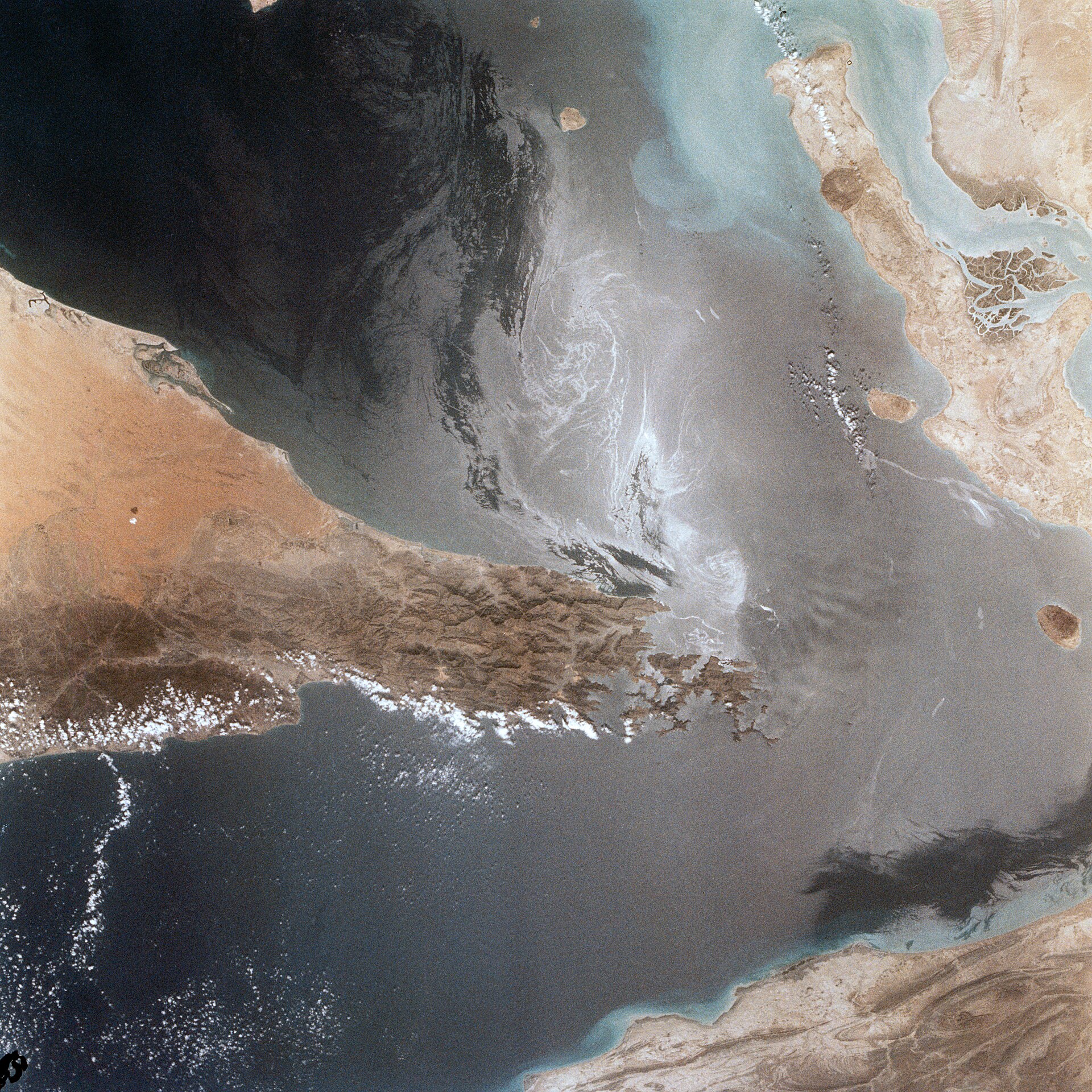 The Strait of Hormuz photographed from the Space Shuttle, showing the narrow waterway between Iran (top) and Oman/UAE (bottom) — the 21-nautical-mile chokepoint through which 20 percent of the world's oil supply transits.