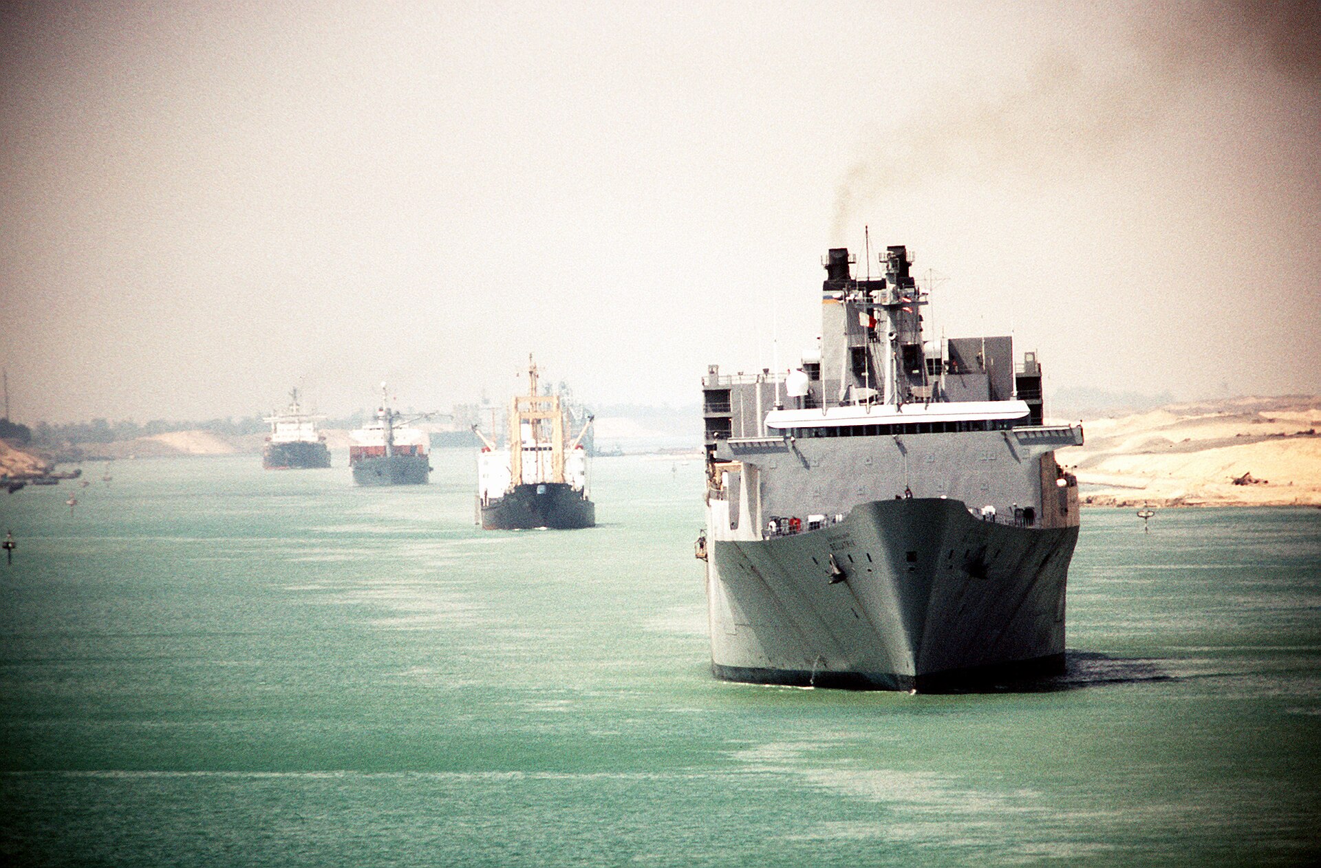 Commercial tankers and the USNS Bellatrix transiting the Suez Canal in 1990 under Egyptian Suez Canal Authority administration — the waterway that Egypt nationalized in 1956 and has administered continuously for 69 years without a dissolution treaty
