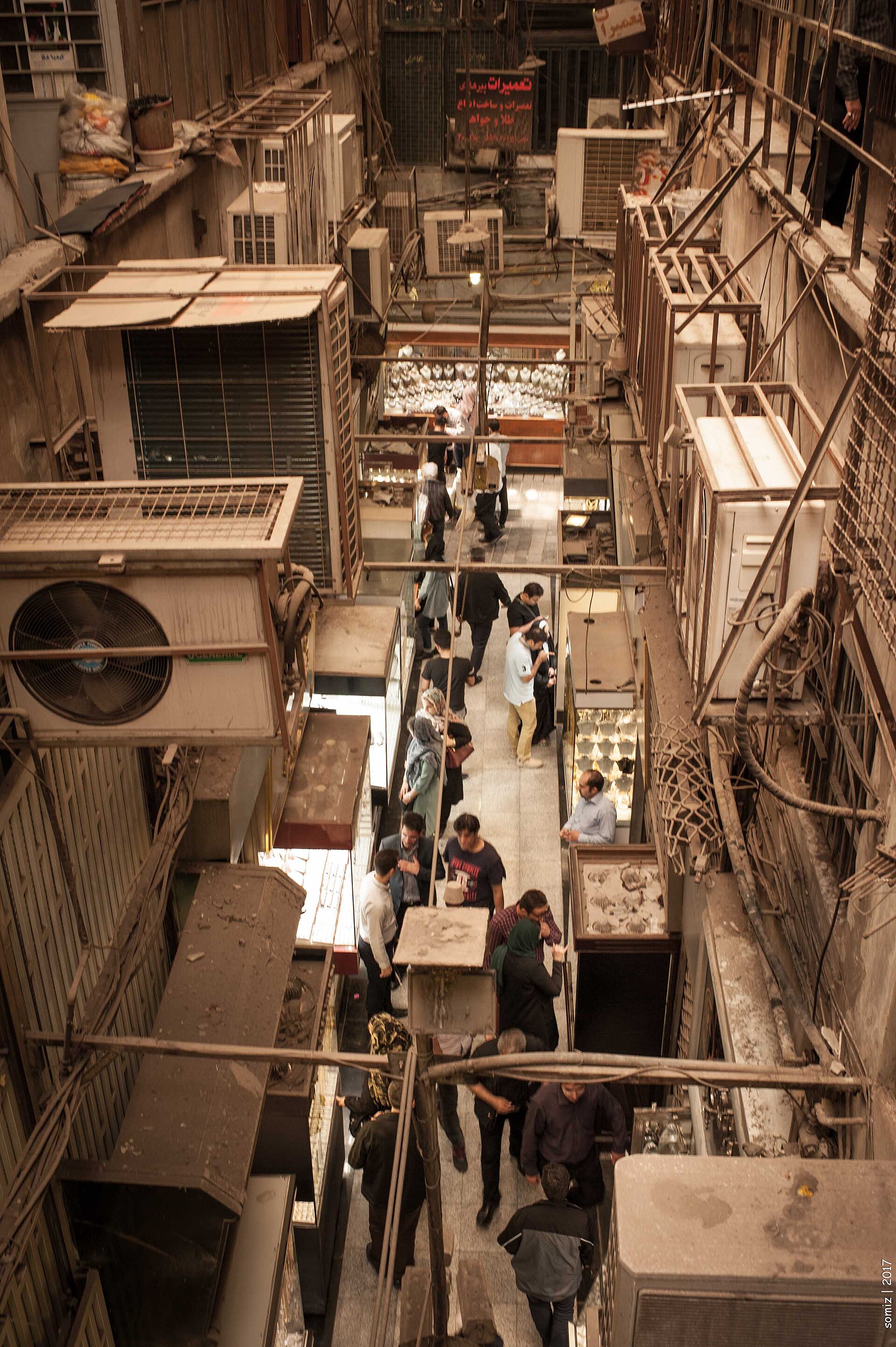 Overhead view of Tehran Grand Bazaar shoppers and merchants in 2017, representing the civilian economy bearing 115 percent food inflation with no institutional mechanism to translate suffering into policy change