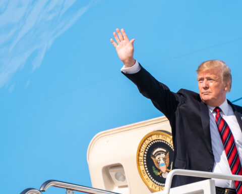 President Trump waving from the stairs of Air Force One at Joint Base Andrews, Presidential seal visible on aircraft door