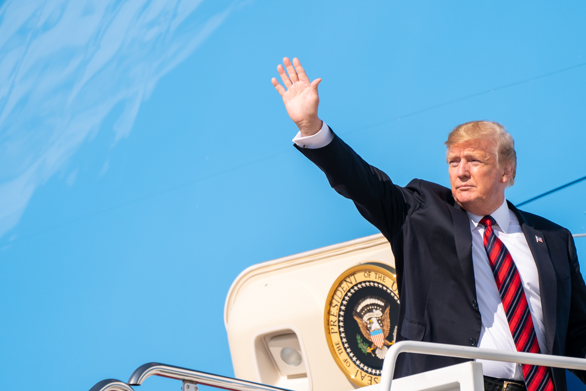 President Trump waving from the stairs of Air Force One at Joint Base Andrews, Presidential seal visible on aircraft door