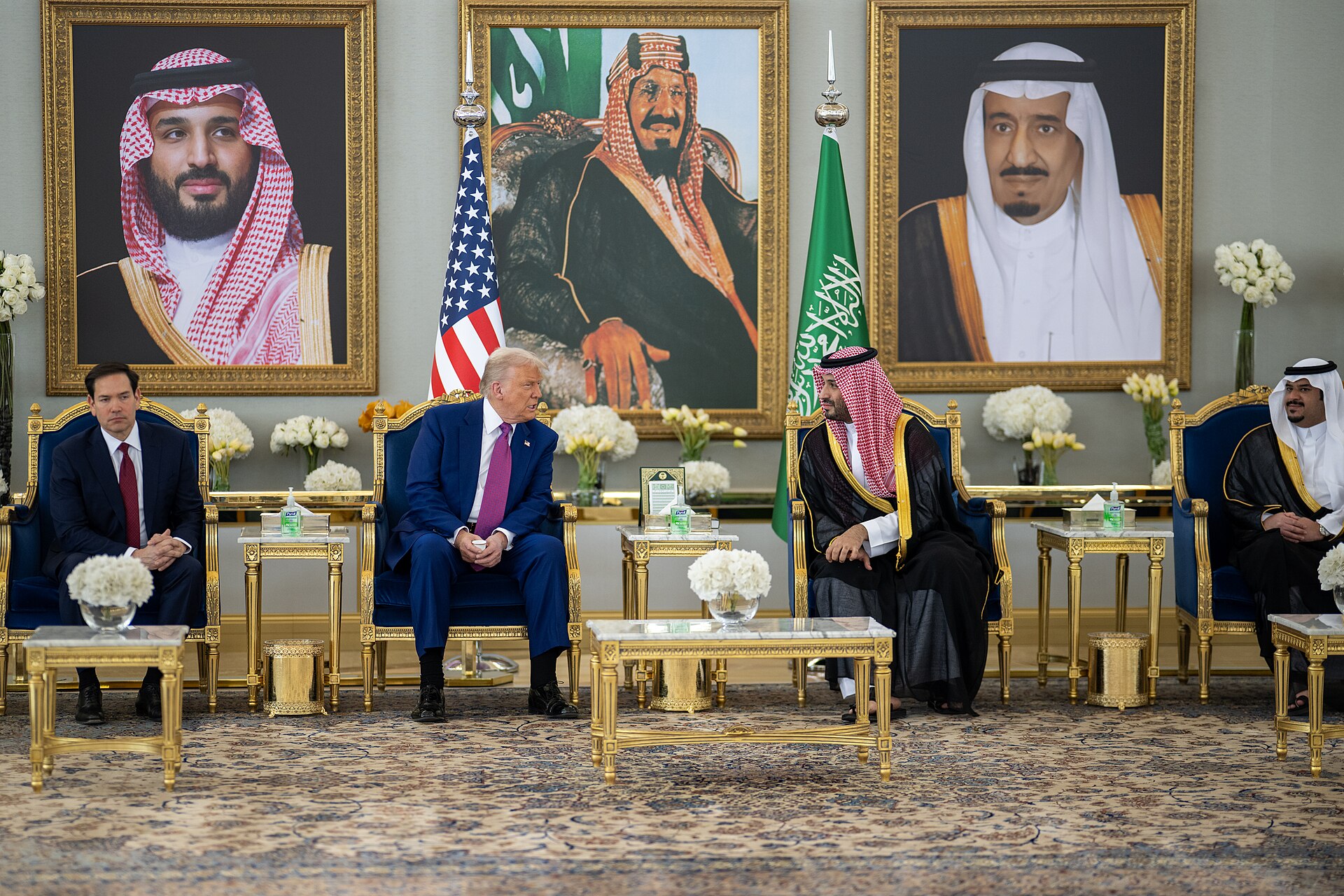 Trump and MBS seated in a Saudi royal palace reception room, May 2025, with portraits of King Salman and MBS on the wall behind them
