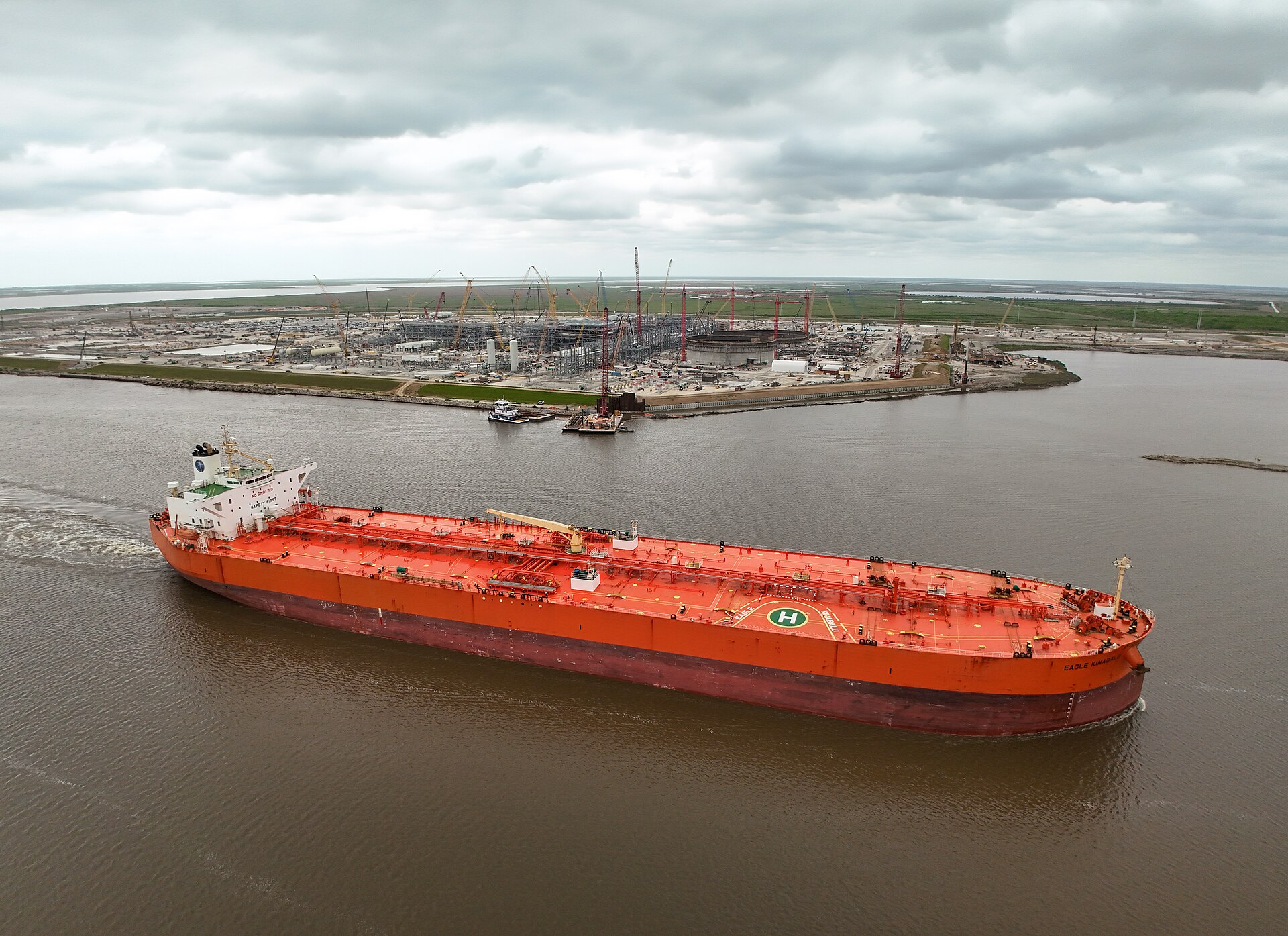 A crude oil tanker transits the Port Arthur, Texas ship channel past an industrial refinery and LNG terminal under construction on the US Gulf Coast
