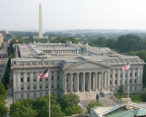 US Treasury Department building Washington DC with American flags and Washington Monument in background