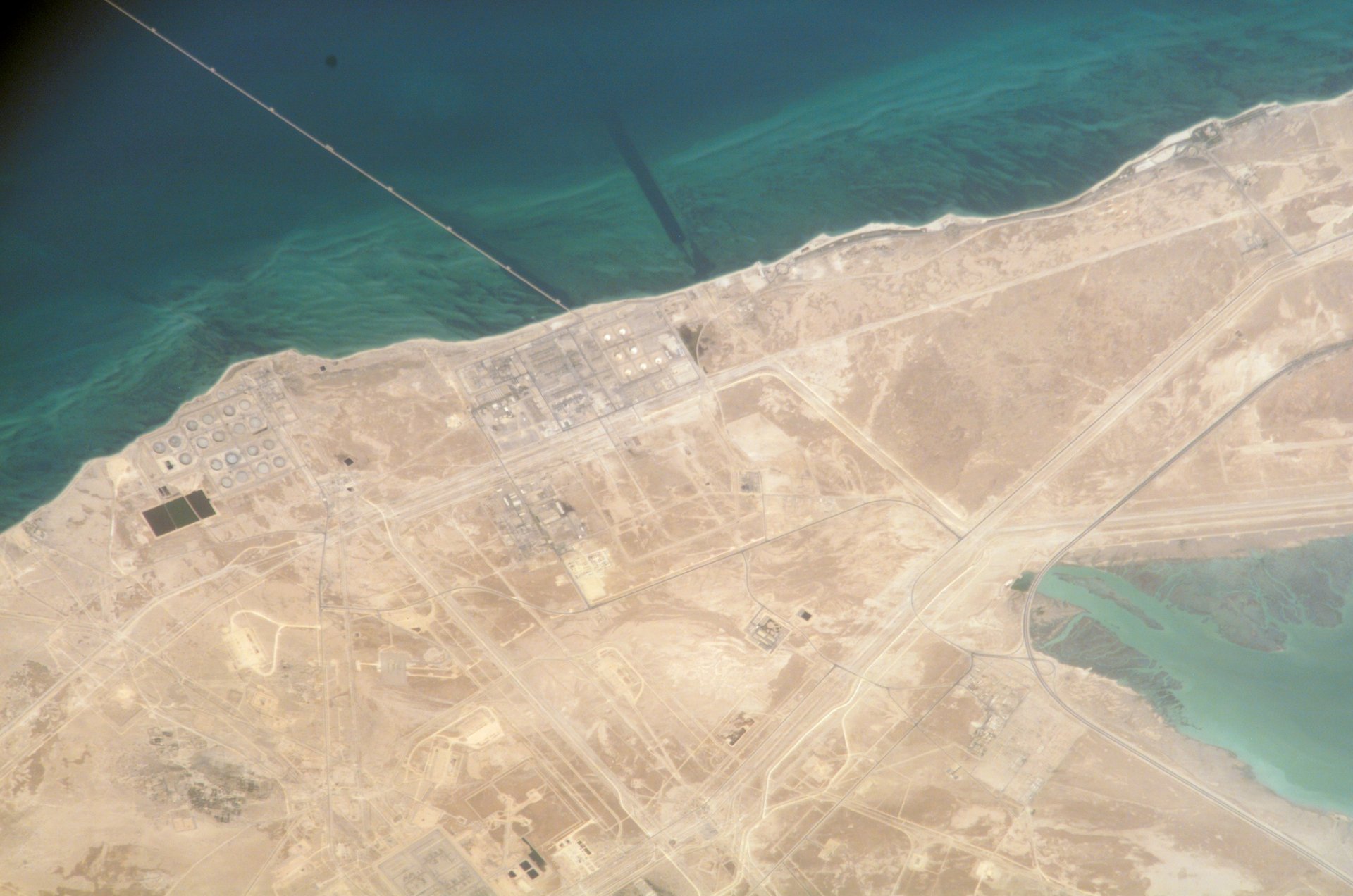 ISS astronaut photograph of Yanbu industrial city and oil terminal on Saudi Arabia's Red Sea coast, showing storage tank farms and port infrastructure serving as the western endpoint of the East-West Pipeline