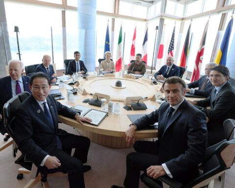 G7 summit leaders seated at round table, Hiroshima 2023, with national flags and Macron visible at France nameplate