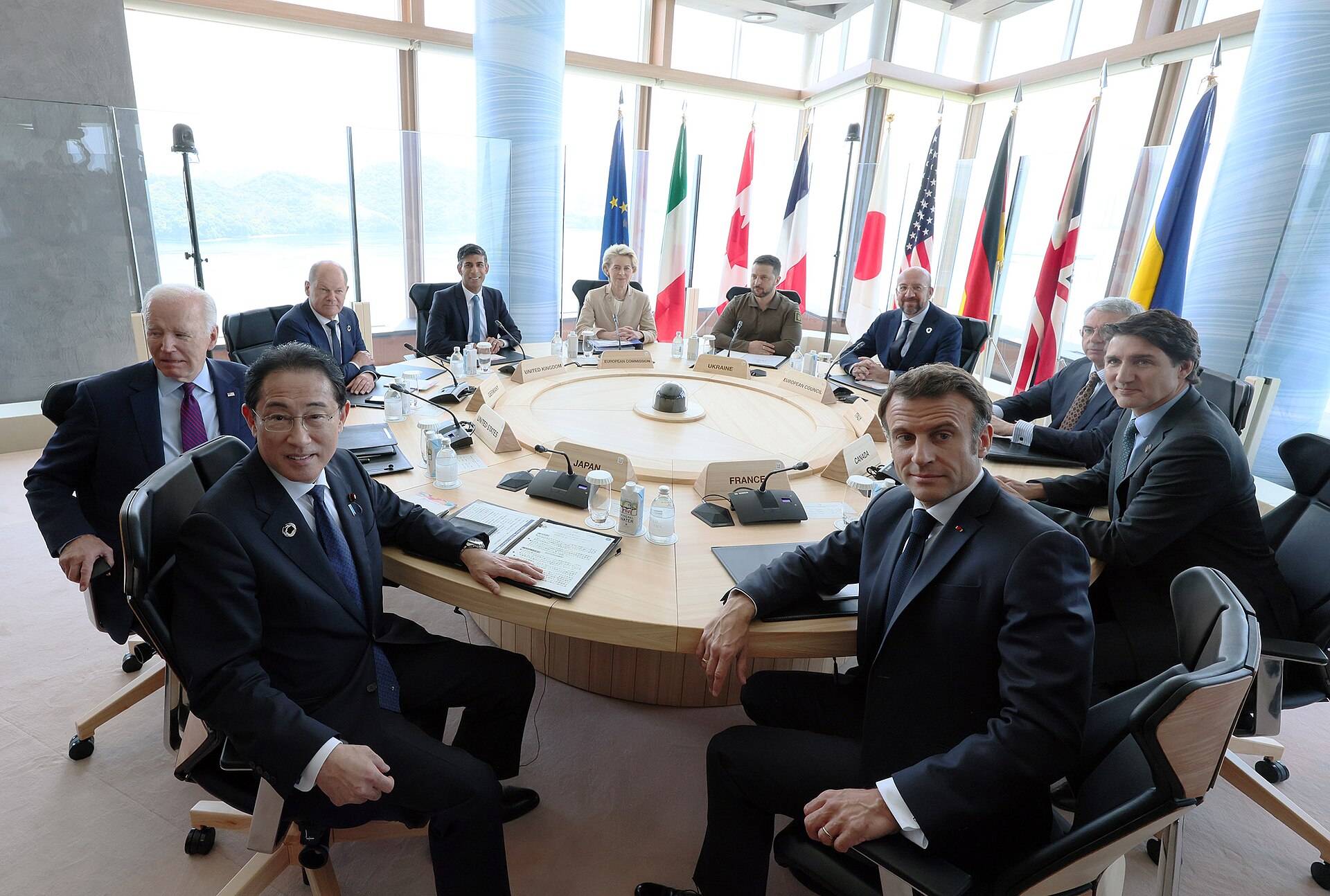 G7 summit leaders seated at round table, Hiroshima 2023, with national flags and Macron visible at France nameplate