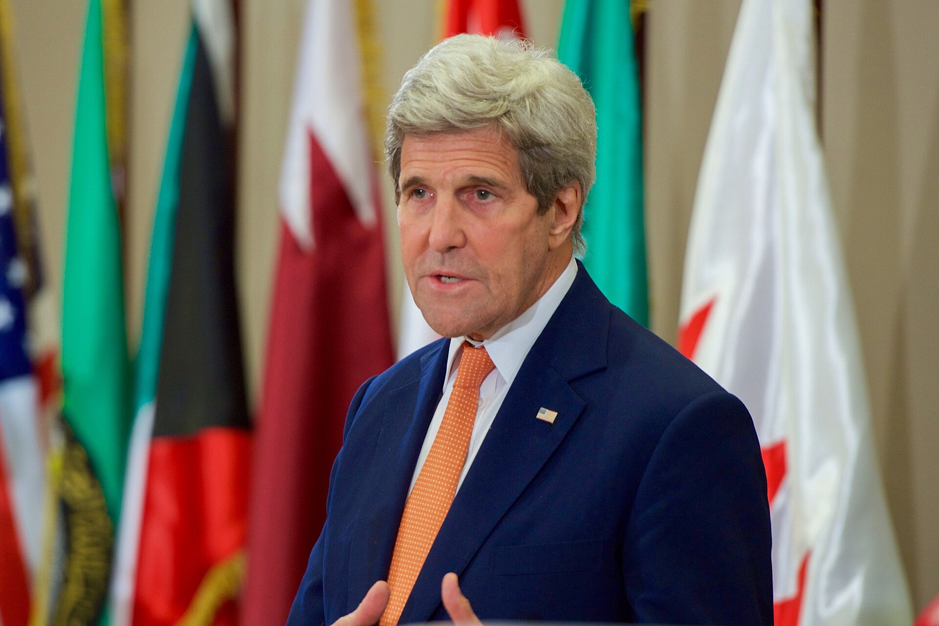 US Secretary of State Kerry at a GCC Ministerial Council meeting in Manama, Bahrain, with GCC member state flags — Qatar, Kuwait, UAE, Saudi Arabia, Bahrain visible — the US-GCC alliance architecture that Baghdad's eight-party framework explicitly excludes by design