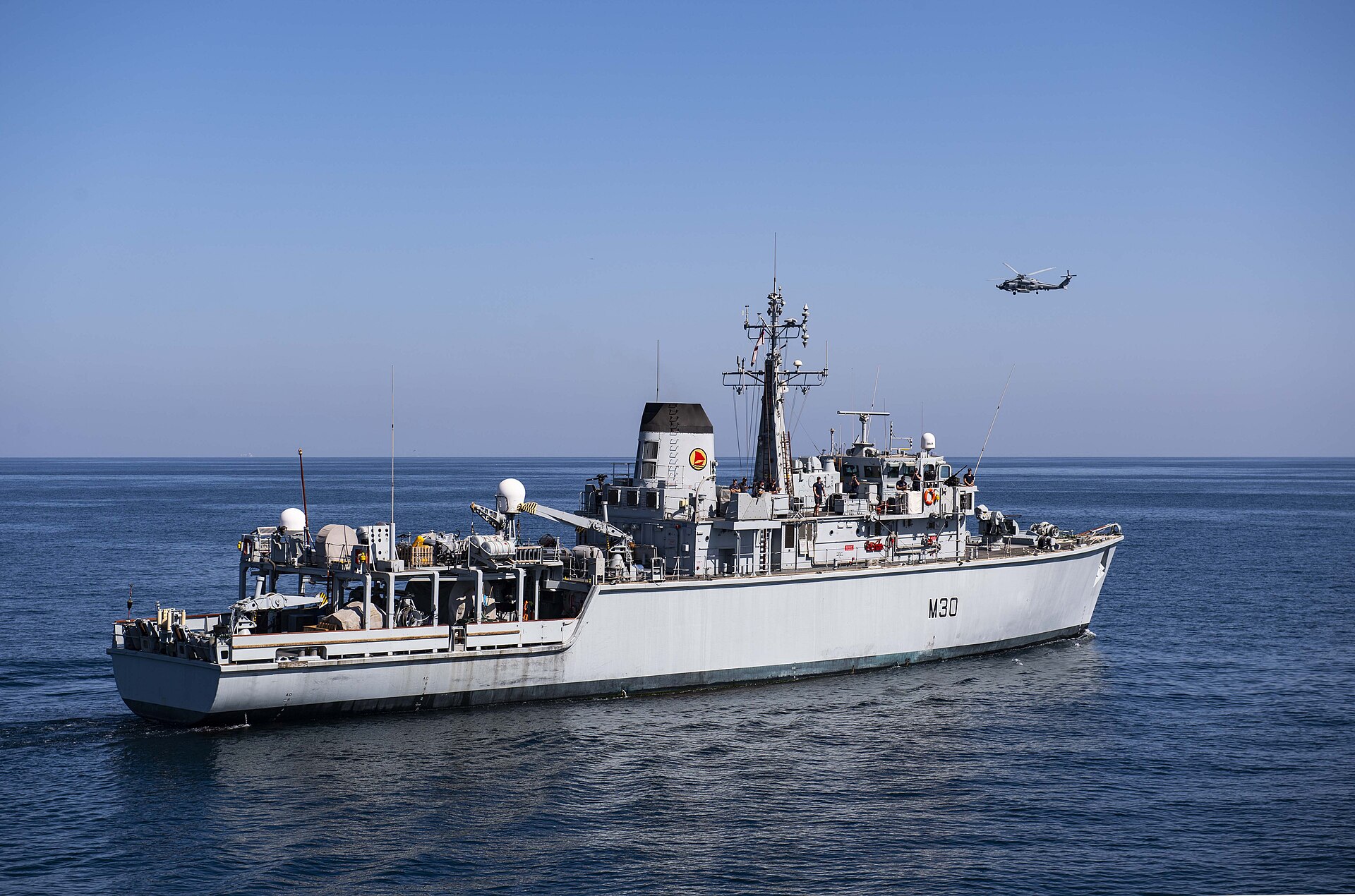 Royal Navy mine countermeasures vessel HMS Ledbury M30 underway in the Arabian Gulf with a helicopter conducting sweep operations, March 2020