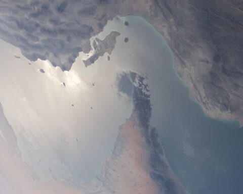 The Strait of Hormuz — the 21-nautical-mile passage between Iran and Oman — photographed from the International Space Station during Expedition 64, March 2021. The PGSA-designated Qeshm-Larak corridor for inbound traffic runs inside Iran's claimed 12-nautical-mile territorial sea, visible along the upper coastline. Photo: NASA / Public Domain