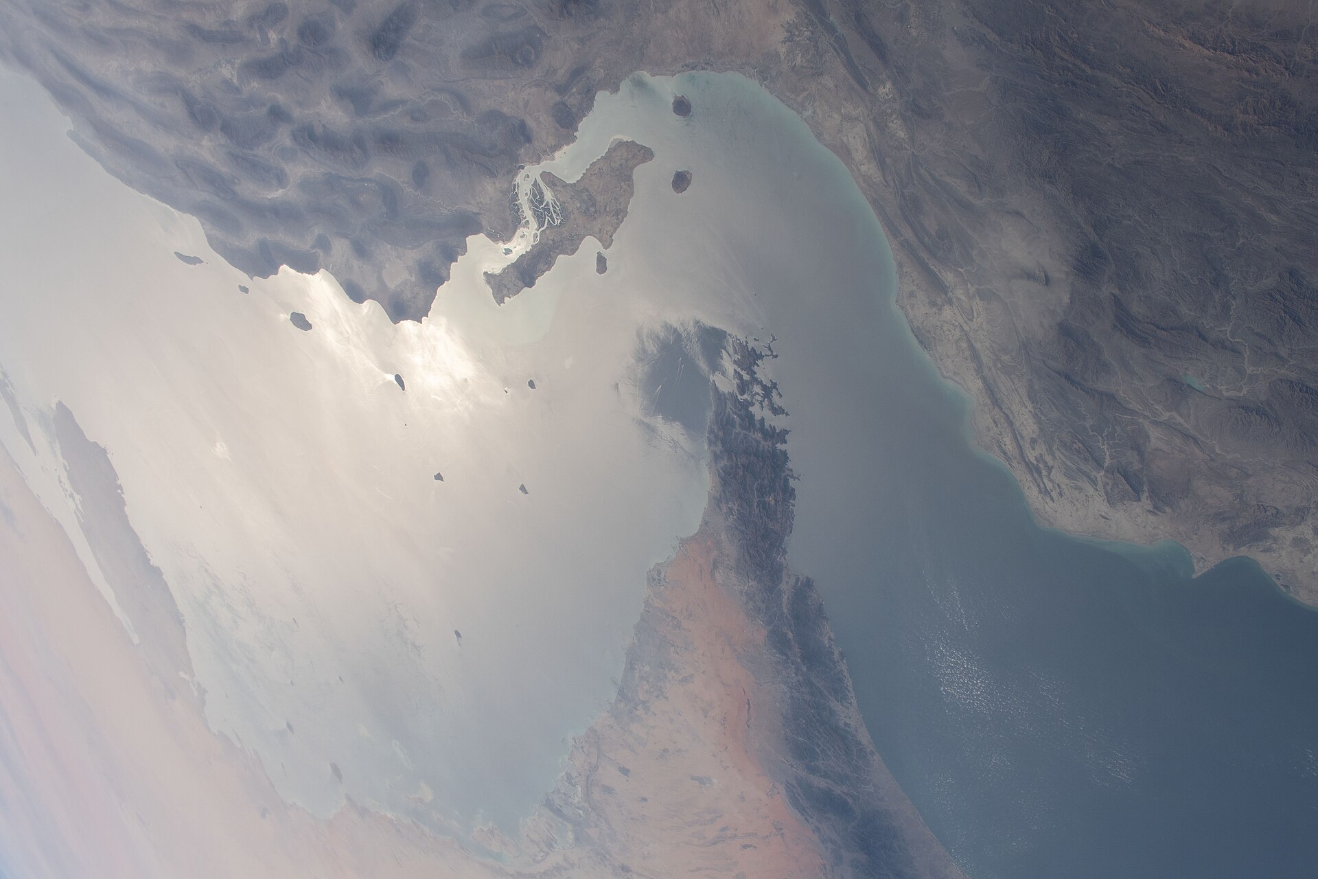 The Strait of Hormuz — the 21-nautical-mile passage between Iran and Oman — photographed from the International Space Station during Expedition 64, March 2021. The PGSA-designated Qeshm-Larak corridor for inbound traffic runs inside Iran's claimed 12-nautical-mile territorial sea, visible along the upper coastline. Photo: NASA / Public Domain