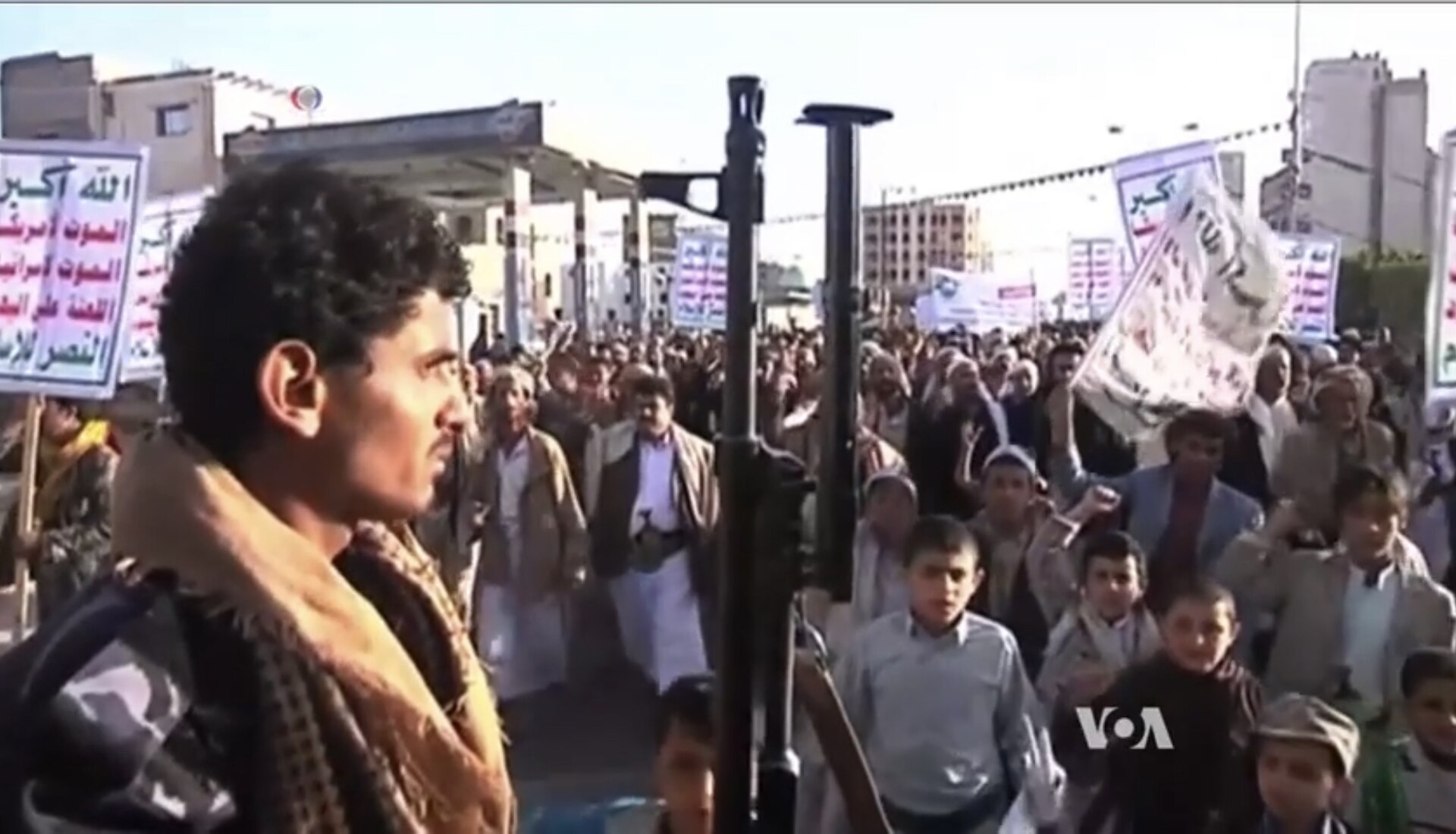 A Houthi gathering in Sanaa, Yemen, with an armed guard in the foreground and supporters carrying Ansarallah slogan banners. The movement that declared a total ban on Israeli maritime navigation in the Red Sea on June 8, 2026, has controlled Sanaa and Yemen's western coastline since 2014.