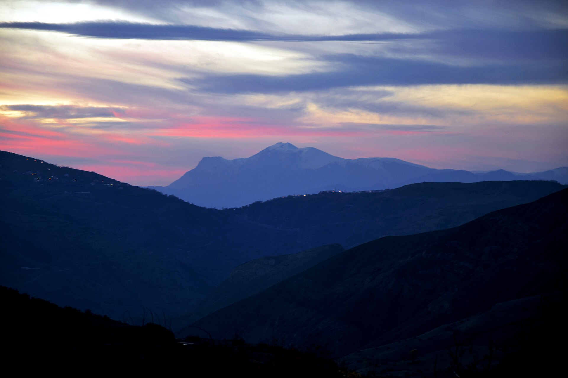 Twilight view of layered mountain ranges in northern Iran near Deylaman, Alborz region, showing remote terrain and isolated access roads