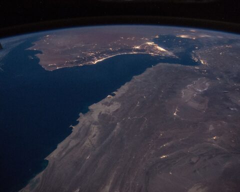 Gulf of Oman and Strait of Hormuz at night photographed from the International Space Station during Expedition 46, showing the Iranian coast lit from above as the pinch point between the Persian Gulf and open ocean