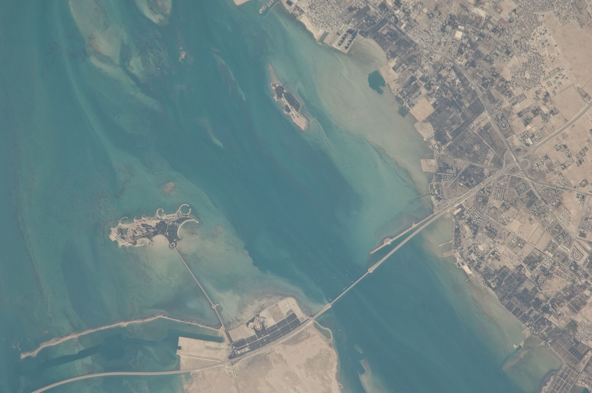 NASA International Space Station photograph of the King Fahd Causeway linking Saudi Arabia (right) to Bahrain (left) across the Gulf. Bahrain's Patriot batteries provide a forward intercept layer for the same threat azimuths covering Saudi Aramco facilities in the Eastern Province, 25 kilometers away.