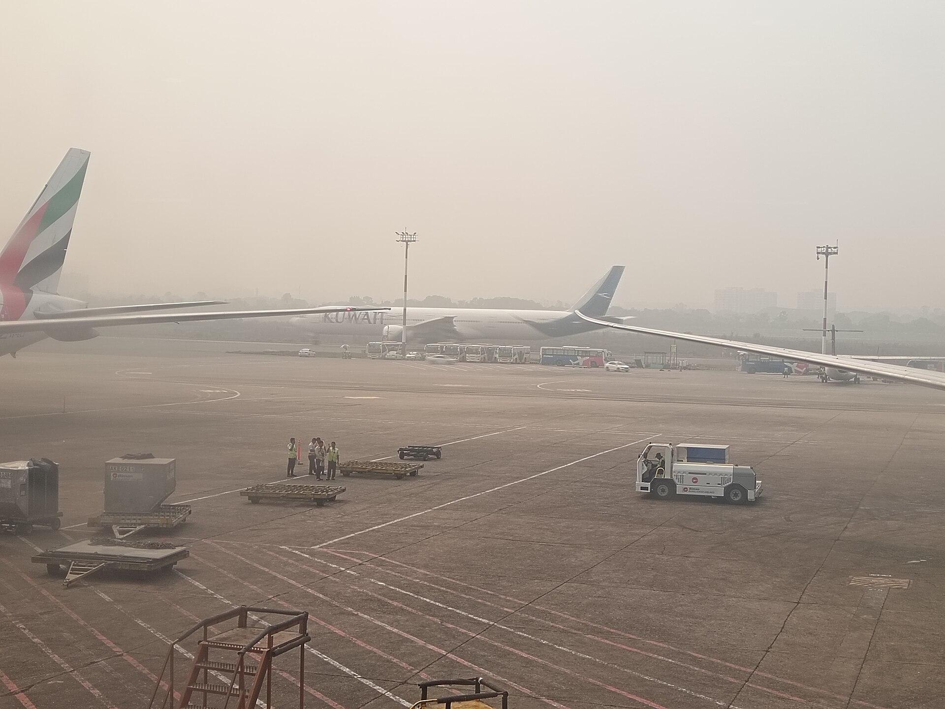 Kuwait Airways Boeing 777 and Emirates aircraft on the apron at Dhaka Airport in April 2026 — Gulf commercial carriers operating weeks before Terminal 1 in Kuwait was struck by Iranian drones