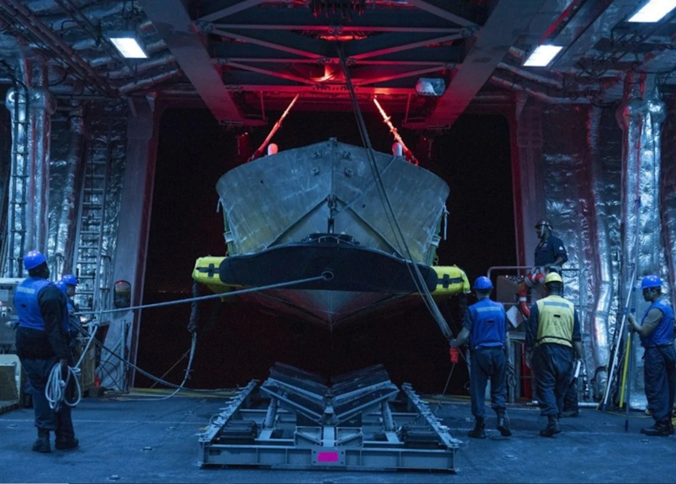 Mine countermeasures unmanned underwater vehicle in the mission bay of a US Navy Independence-class littoral combat ship, with crew preparing it for deployment