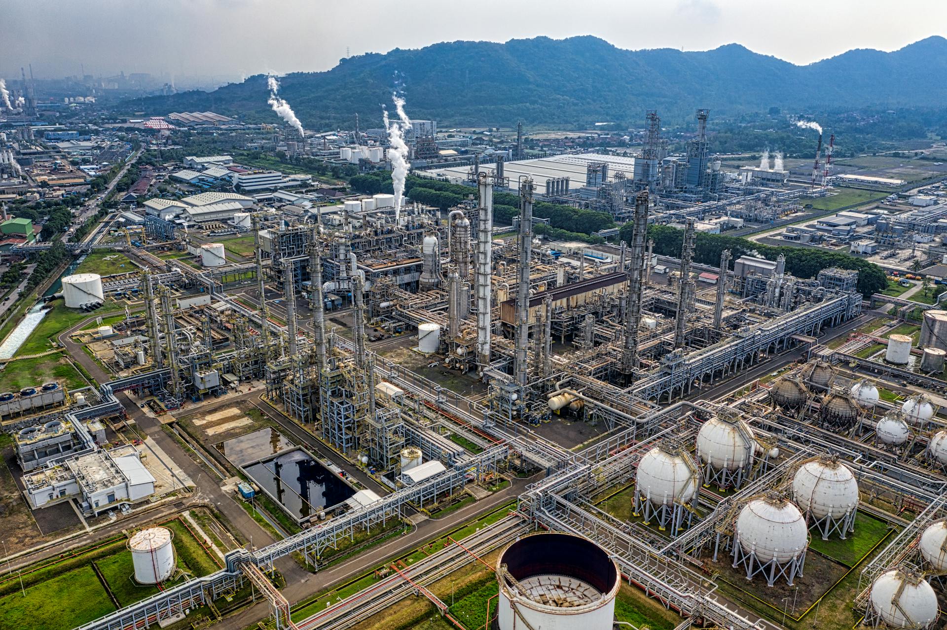 Aerial view of a large oil refinery with distillation towers, pipelines, and spherical storage tanks