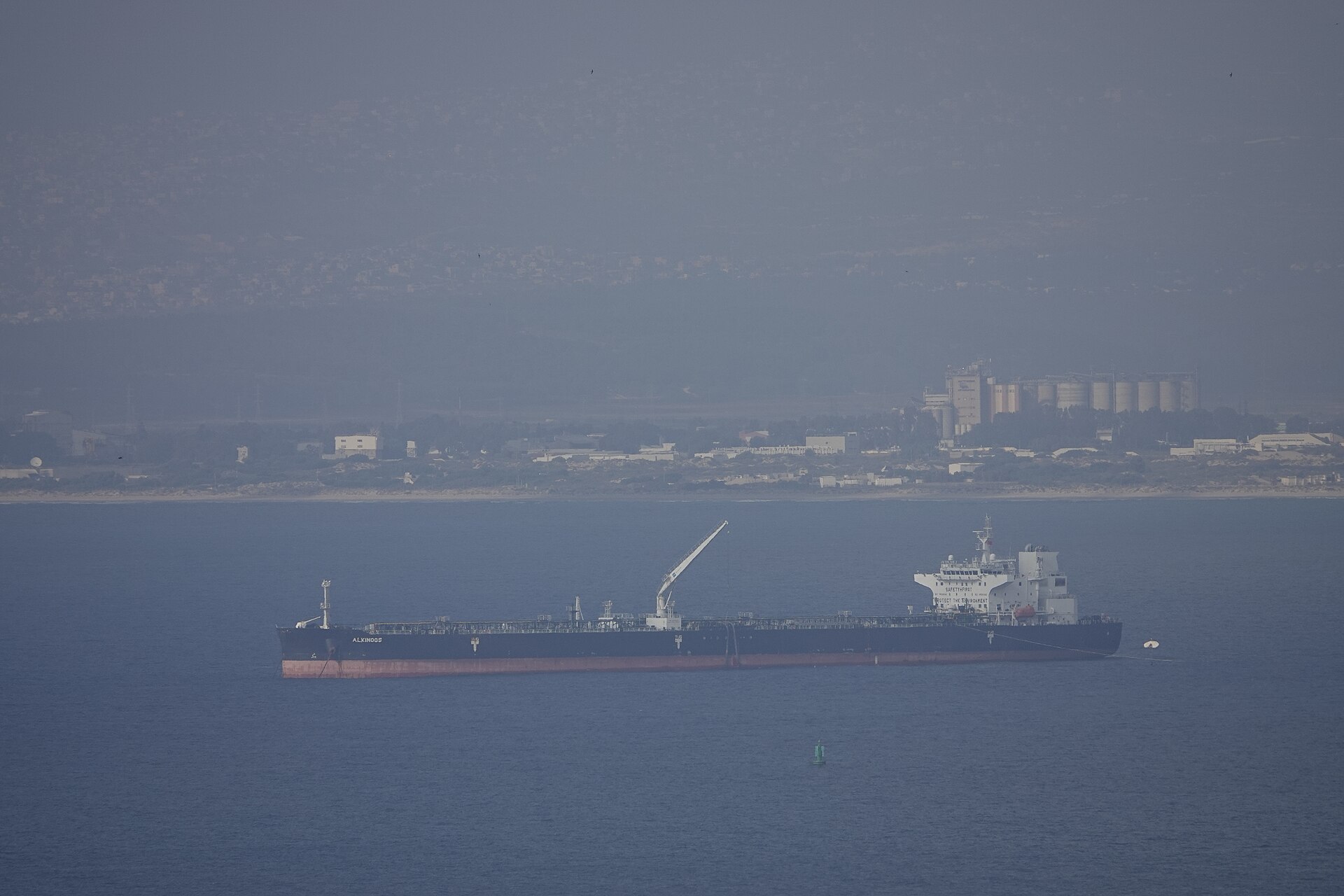 Large crude oil tanker Alkinoos at anchor offshore, illustrating the scale and holding posture of VLCCs waiting for commercial insurance clearance before transit
