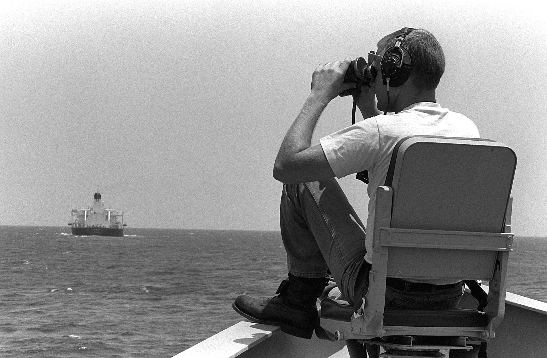 A lookout aboard a US Navy vessel watches an oil tanker through binoculars during Operation Earnest Will convoy escort operations in the Persian Gulf, 1987. Photo: Senior Chief POM Mitchell, USN / Public Domain
