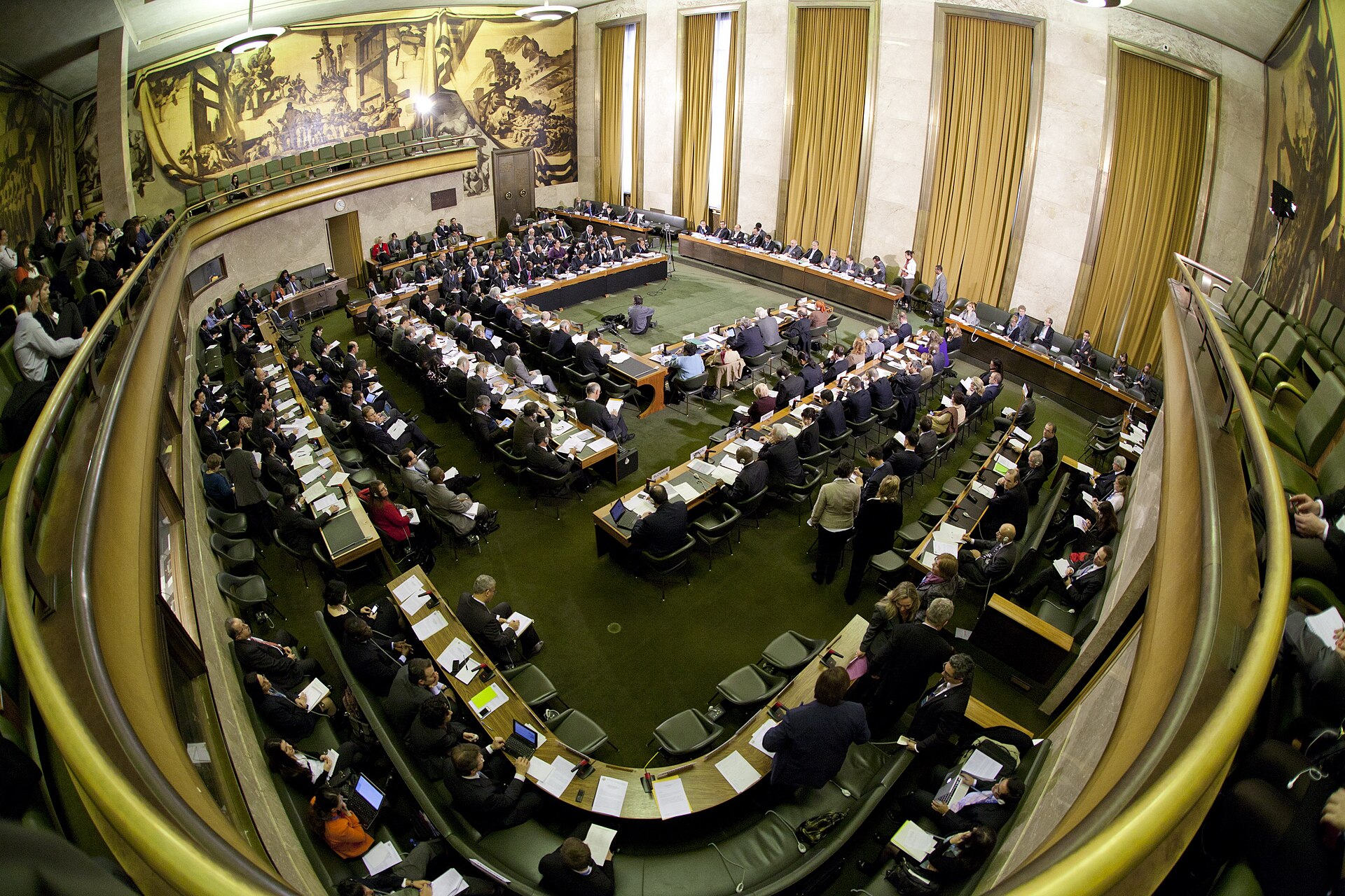 The Council Chamber at the Palais des Nations in Geneva, where the Conference on Disarmament holds its sessions, showing delegates seated at the circular table — the same hall where Phase 2 nuclear talks are expected to convene.