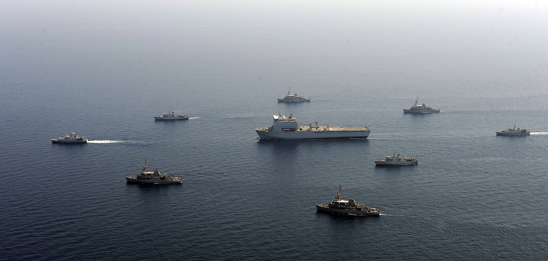RFA Lyme Bay (center) surrounded by eight British and US Navy mine countermeasures ships in the Arabian Sea — the allied coalition now mobilized for Hormuz clearance that Trump told the G7 he did not need.