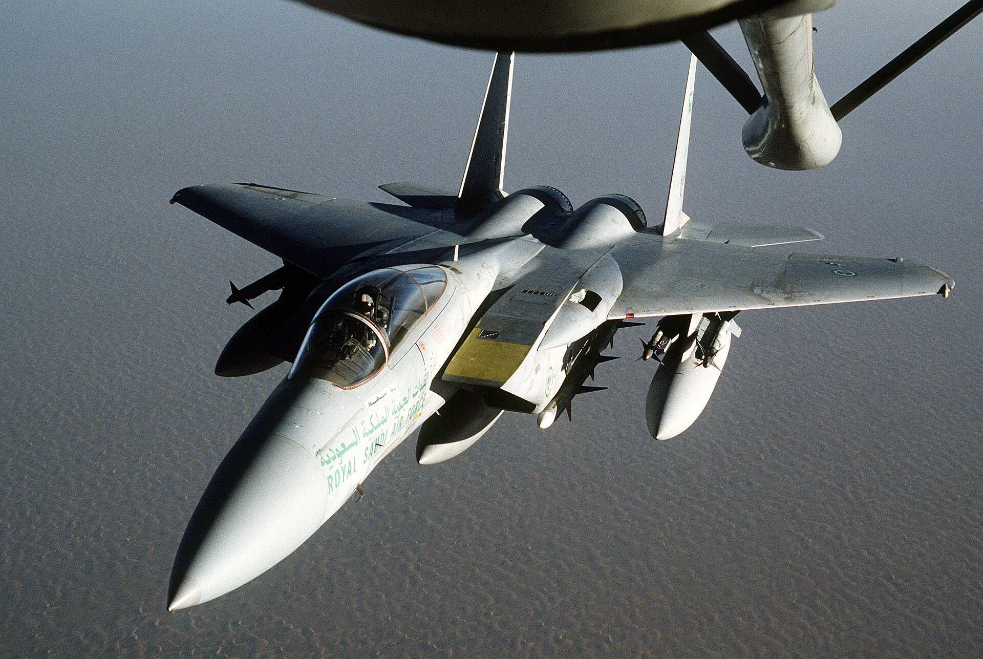 Royal Saudi Air Force F-15 Eagle fighter aircraft approaching a KC-135 tanker for aerial refueling over the Arabian Peninsula desert during Operation Desert Shield — RSAF markings in Arabic and English visible on fuselage