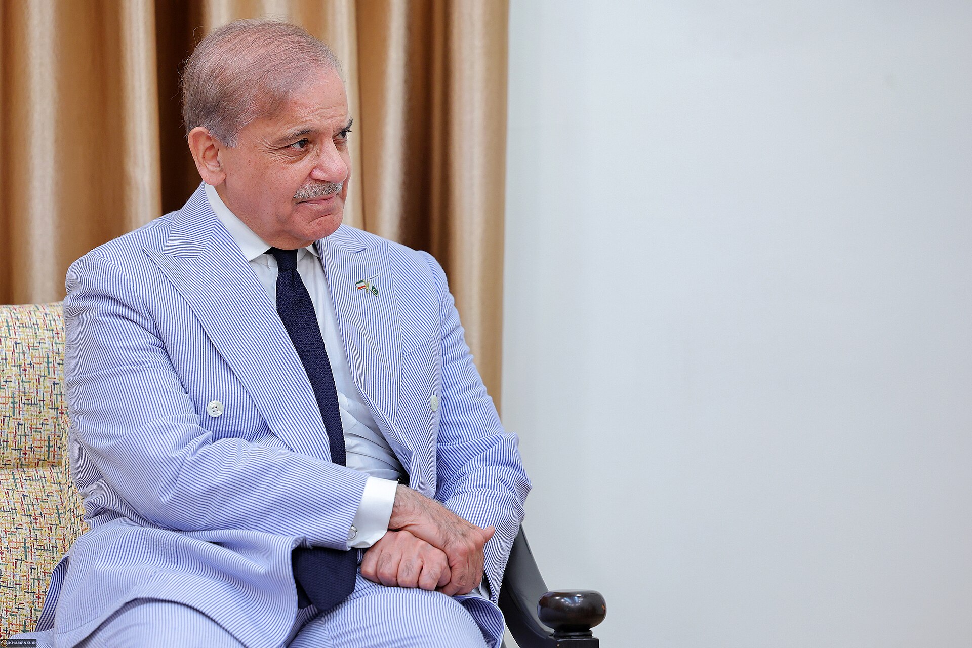 Pakistani Prime Minister Shehbaz Sharif in formal blue pinstripe suit during diplomatic meeting in Tehran, Iran flag pin visible on lapel