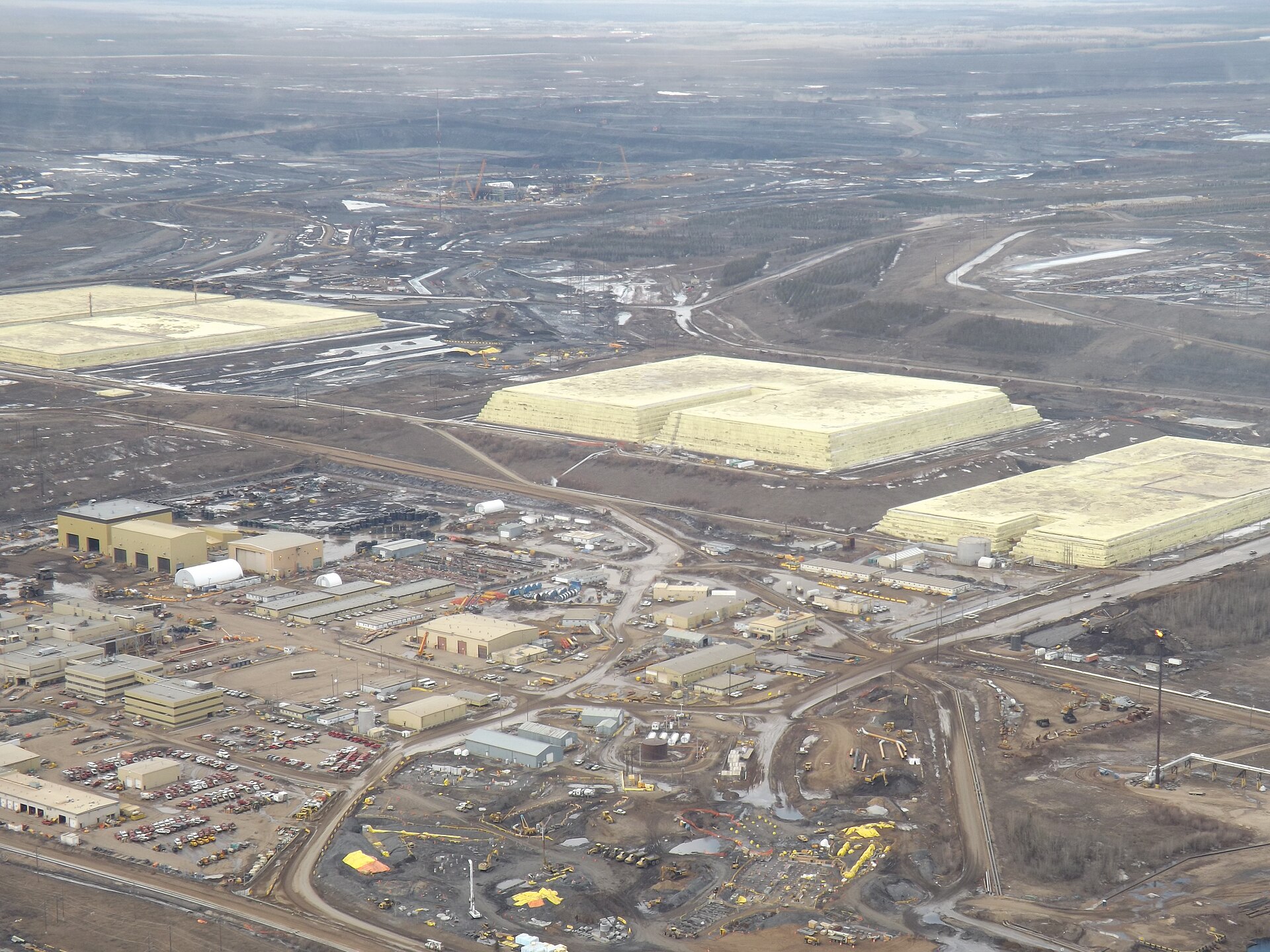 Aerial view of three massive yellow sulfur block pyramids at Syncrude base plant, Alberta Canada — industrial sulfur storage as byproduct of hydrocarbon processing